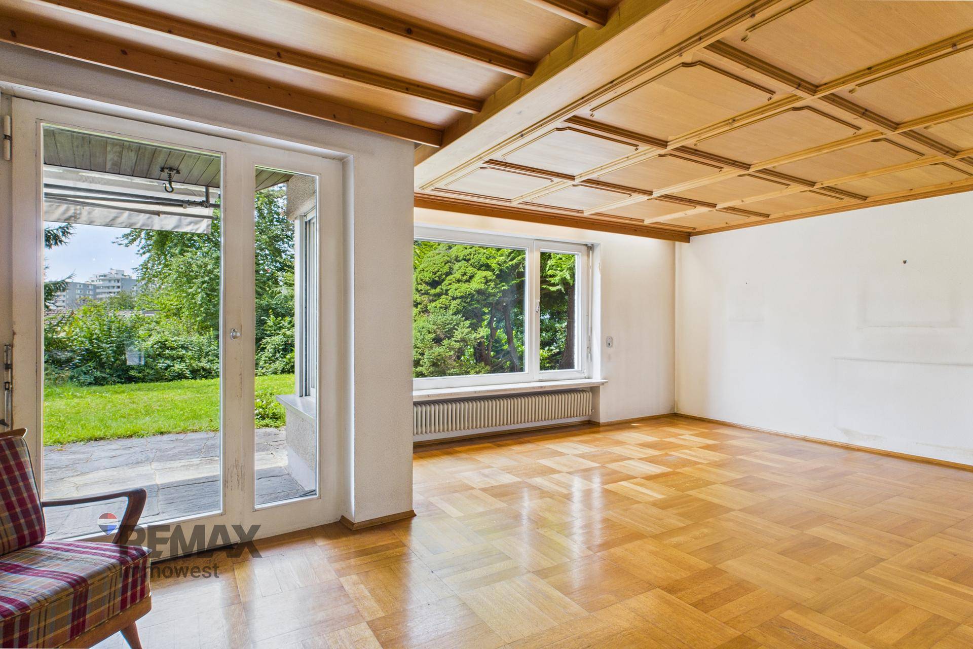 Heller Wohnbereich mit Holzkassettendecke, Parkettboden und Zugang zur Terrasse und Garten.