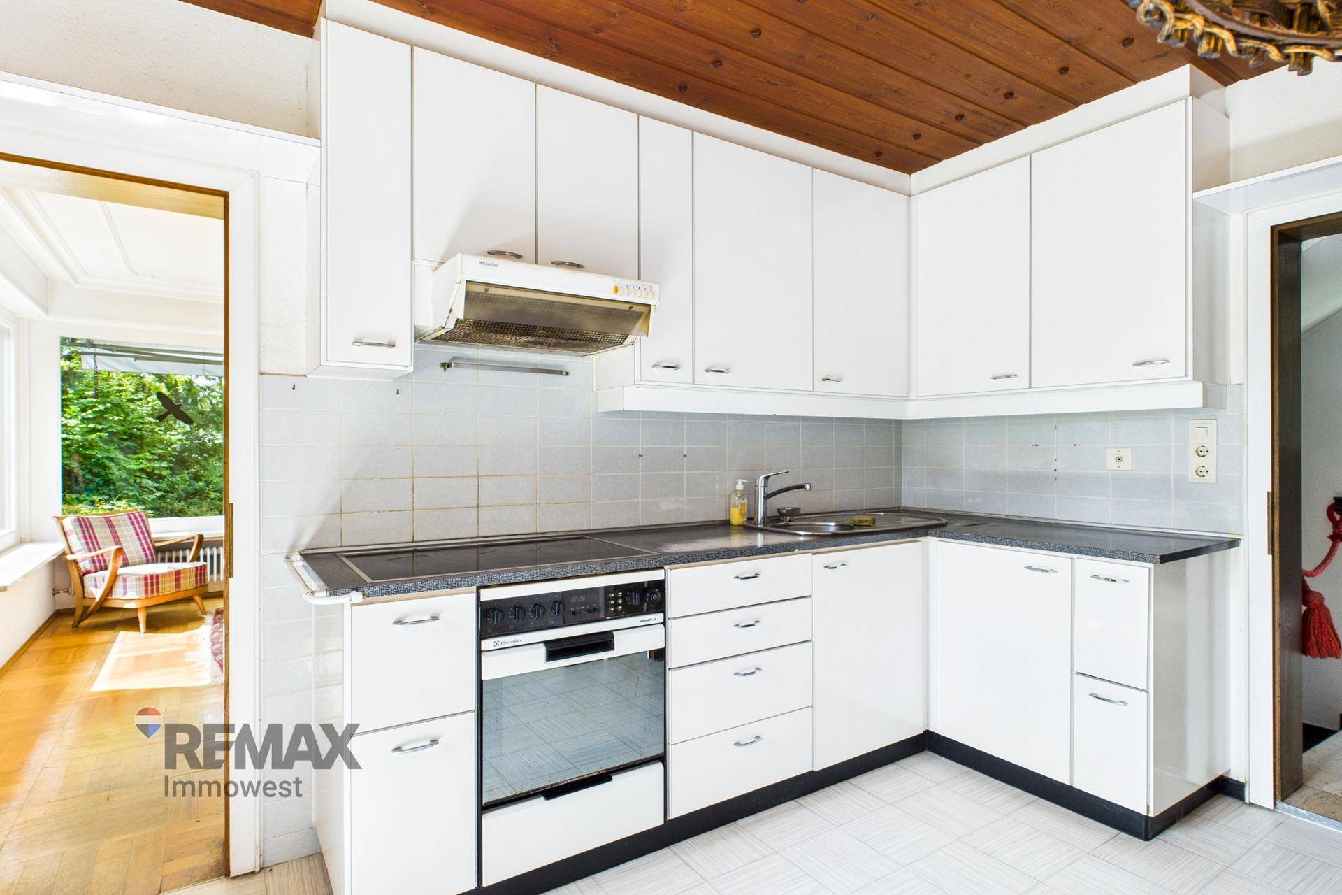 Funktionale Küche mit weißen Schränken, Einbaugeräten und Holzdecke, bereit zur Modernisierung.