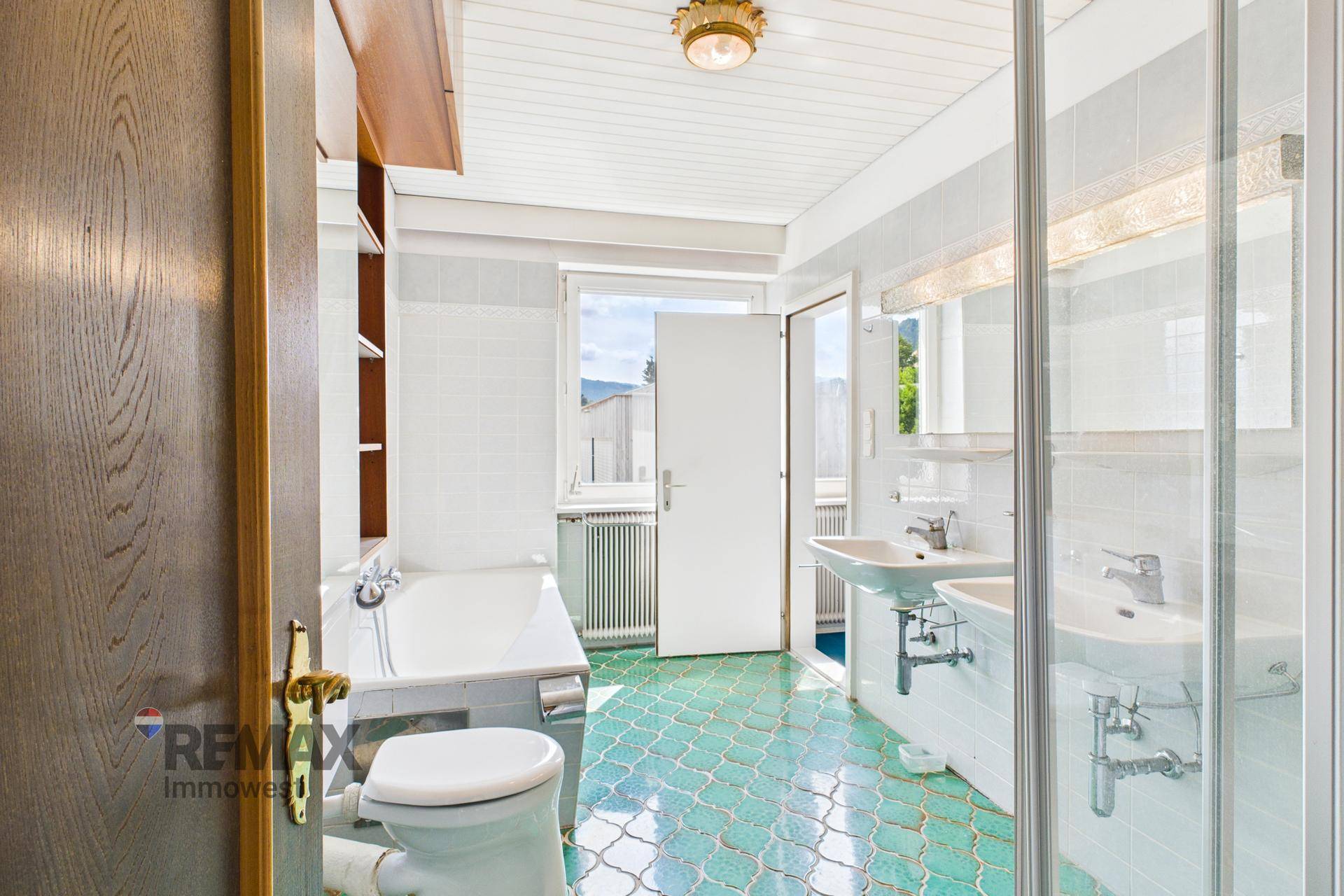 Badezimmer mit Badewanne, Dusche, Doppelwaschbecken und Fenster, ausgestattet mit grünen Fliesen.