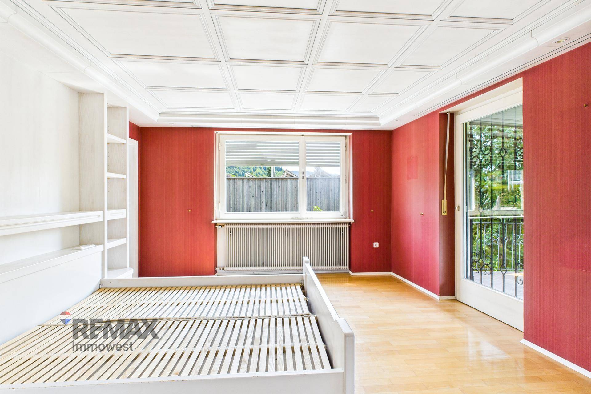 Schlafzimmer mit roter Tapete, Parkettboden und Zugang zu einem französischen Balkon.