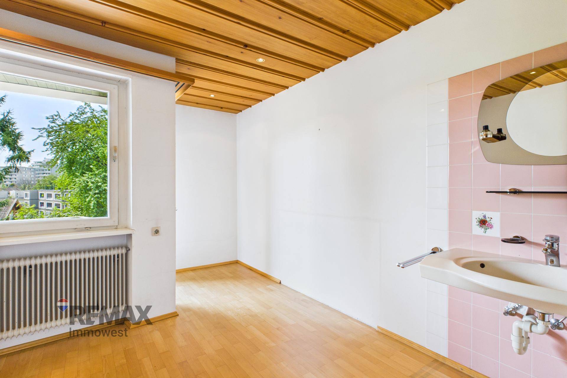 Zimmer mit Parkettboden, Holzdecke und Fenster, ausgestattet mit einem Waschbecken und rosa Fliesen.