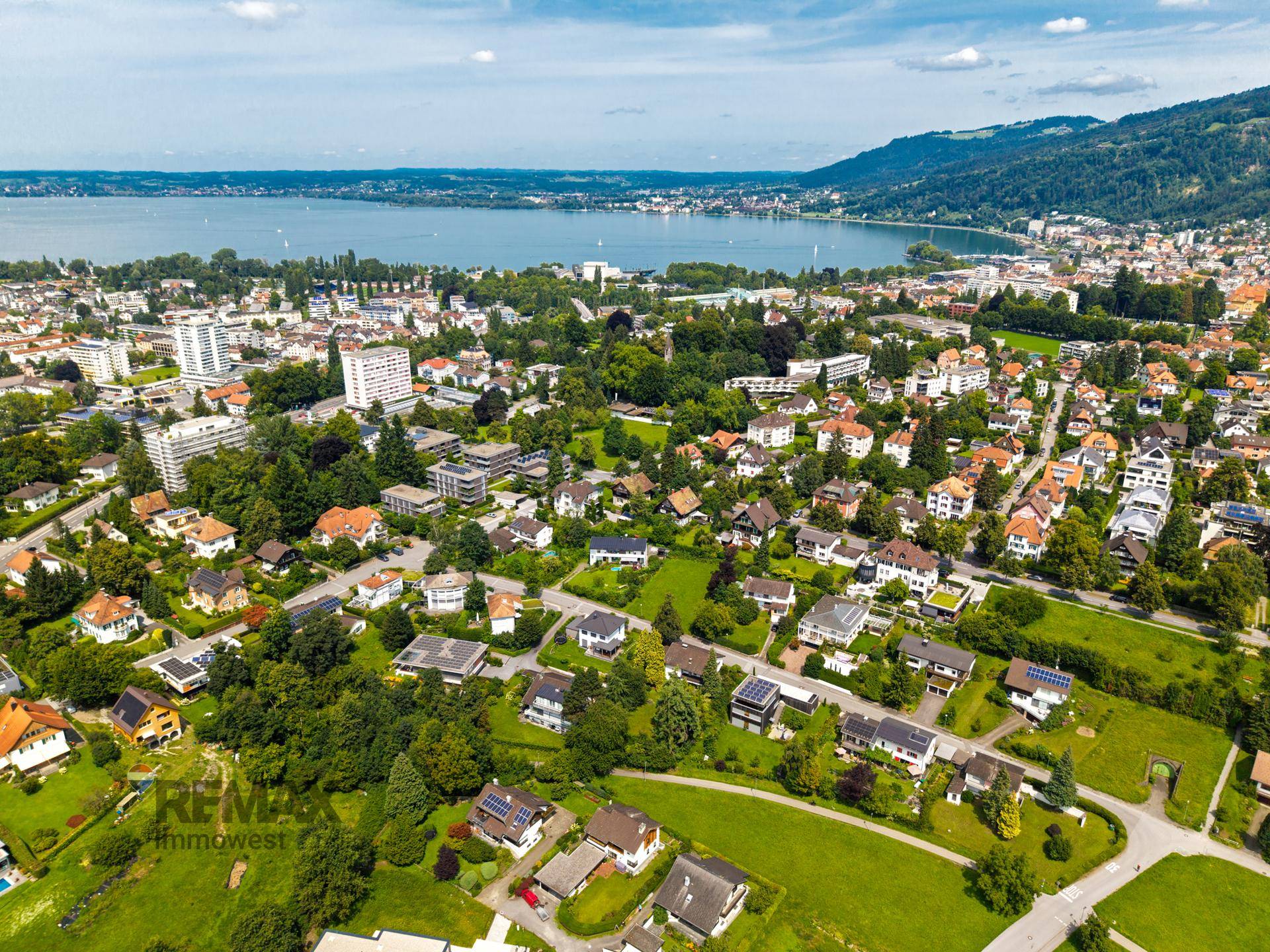 Weitläufige Luftaufnahme einer Stadt am See mit umliegenden Bergen und Wohngebieten.