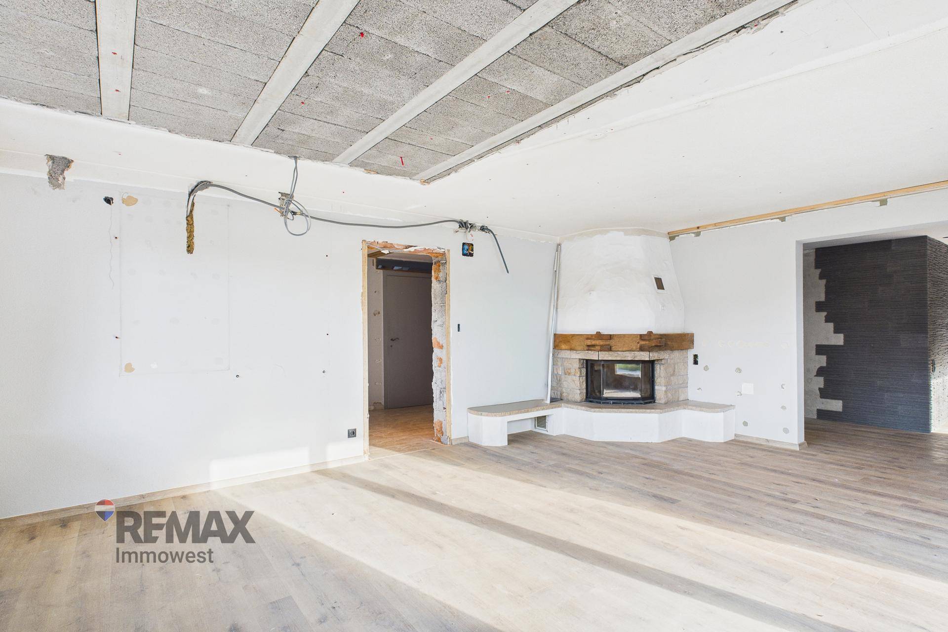 Geräumiges Wohnzimmer im Rohbau mit Kamin und Holzboden, bereit für die Fertigstellung.