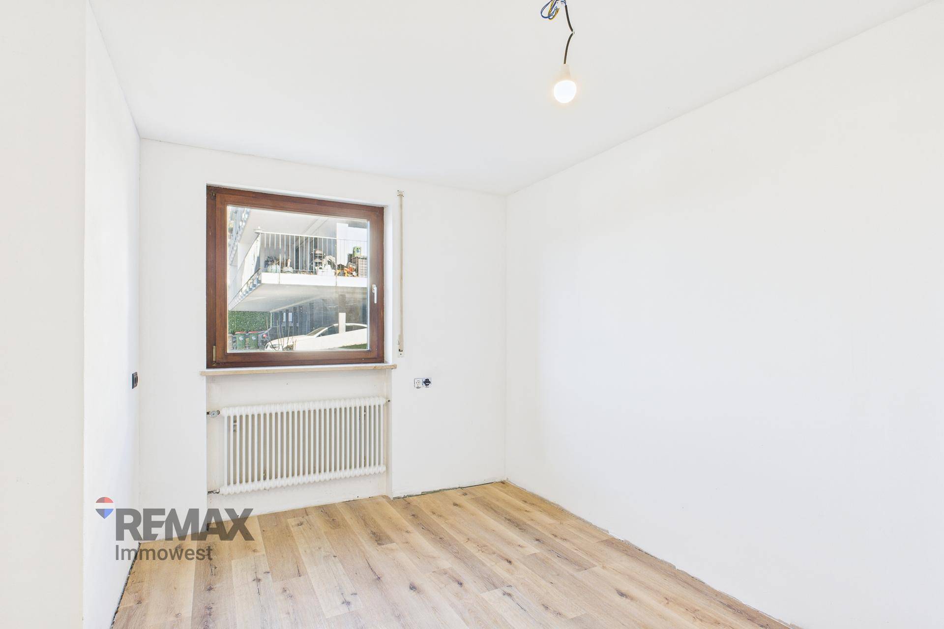 Einfaches Schlafzimmer mit Holzboden und Fenster, das einen Blick auf den Balkon bietet.