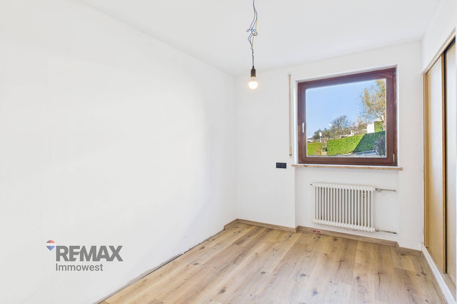 Helles Schlafzimmer mit Holzboden und Fenster, das viel Tageslicht hereinlässt.