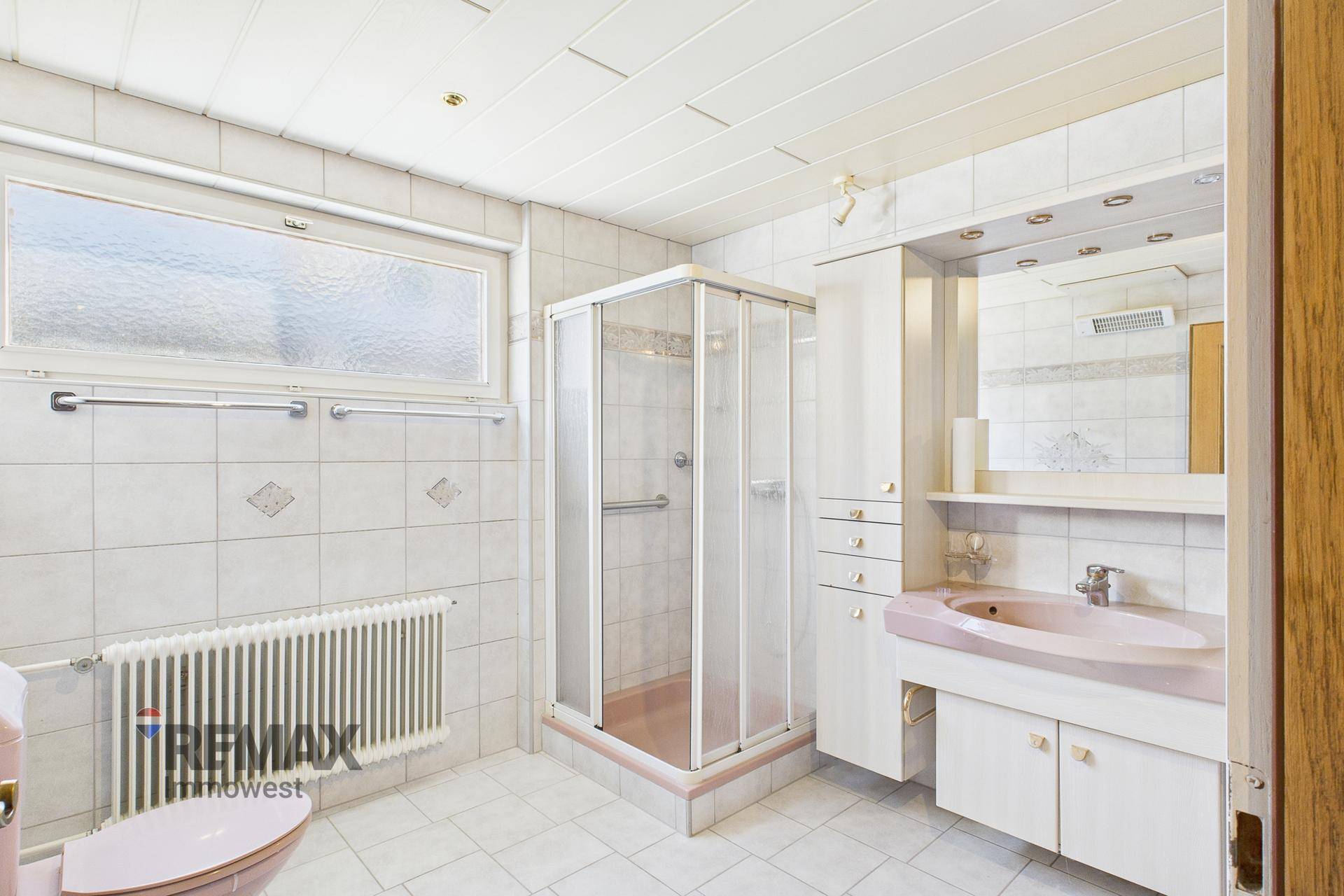 Badezimmer im 80er-Jahre-Stil mit Duschkabine, rosa Waschbecken und weißen Fliesen.
