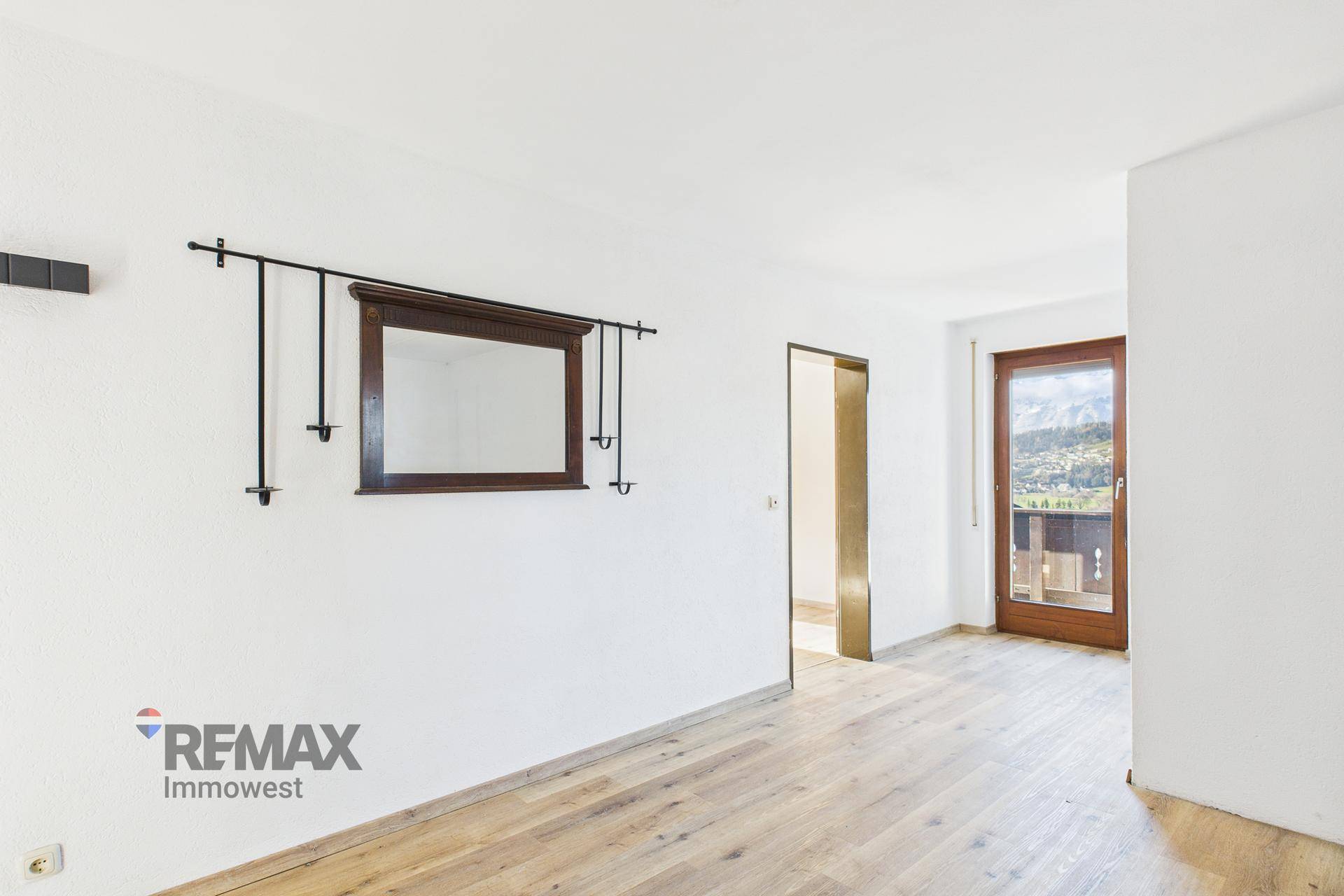 Heller Raum mit Holzboden und Zugang zu einem Balkon, ideal für eine gemütliche Sitzecke.