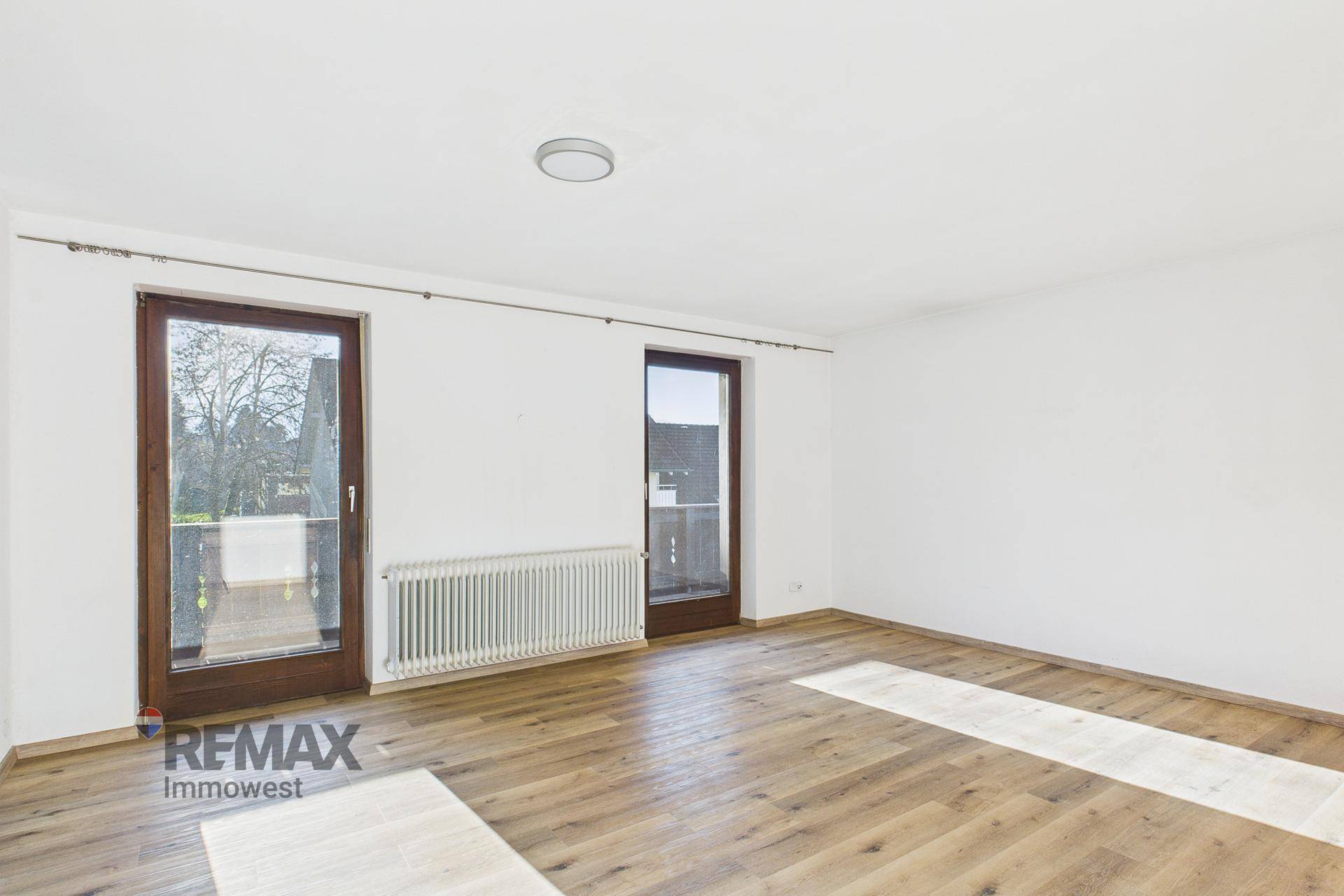 Heller Raum mit Holzboden und zwei Balkontüren, die den Zugang nach draußen ermöglichen.