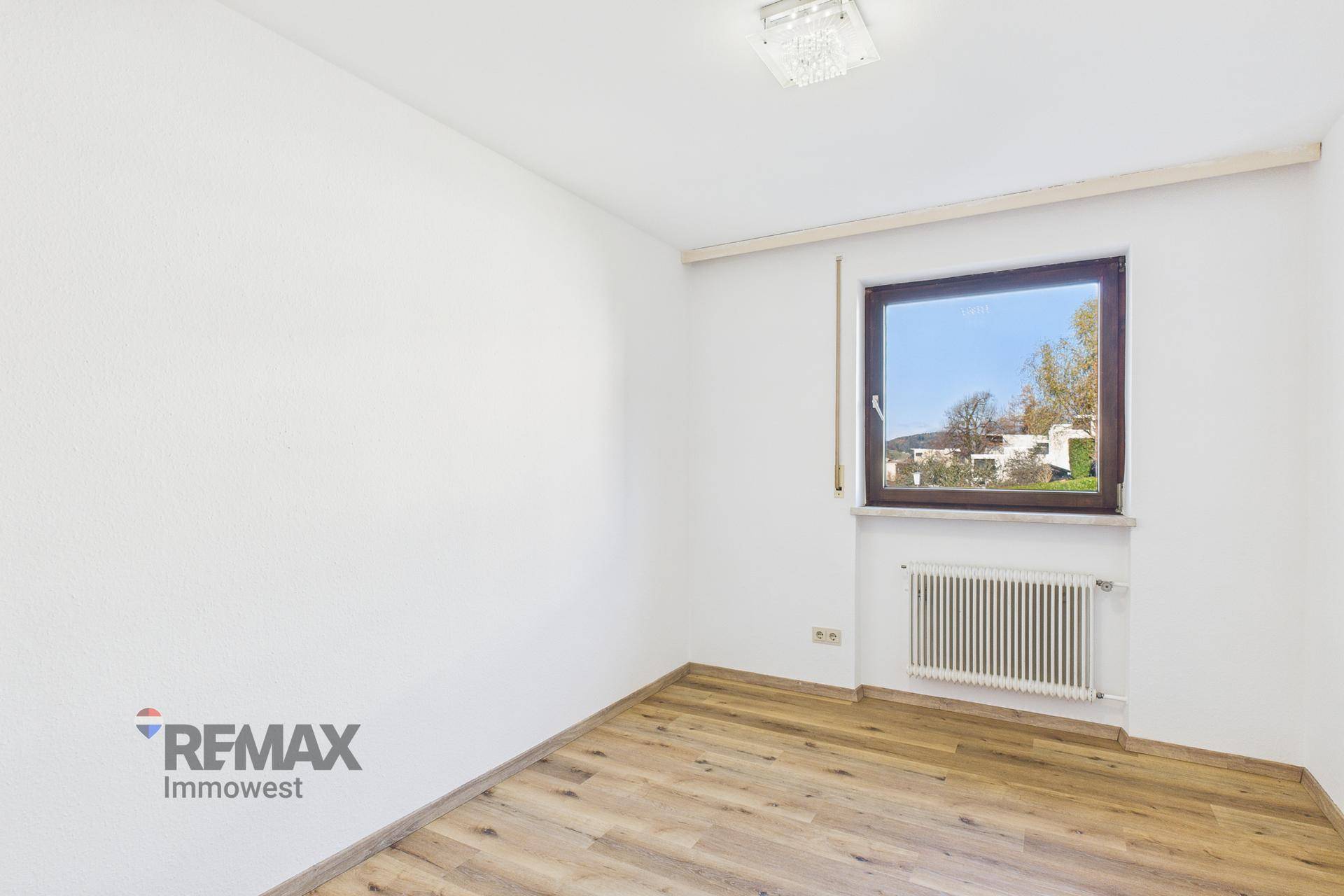 Helles Schlafzimmer mit Holzboden und Fenster, das einen Blick ins Grüne ermöglicht.