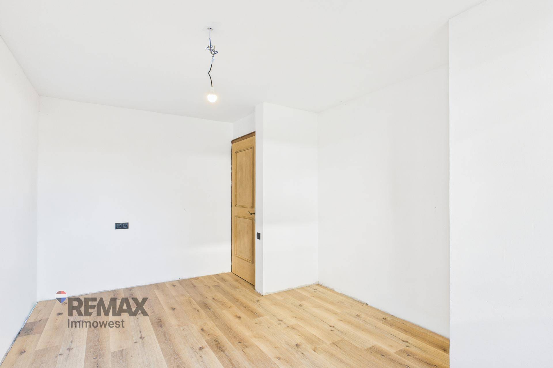 Helles Schlafzimmer mit Holzboden und Fenster, das viel Tageslicht hereinlässt.