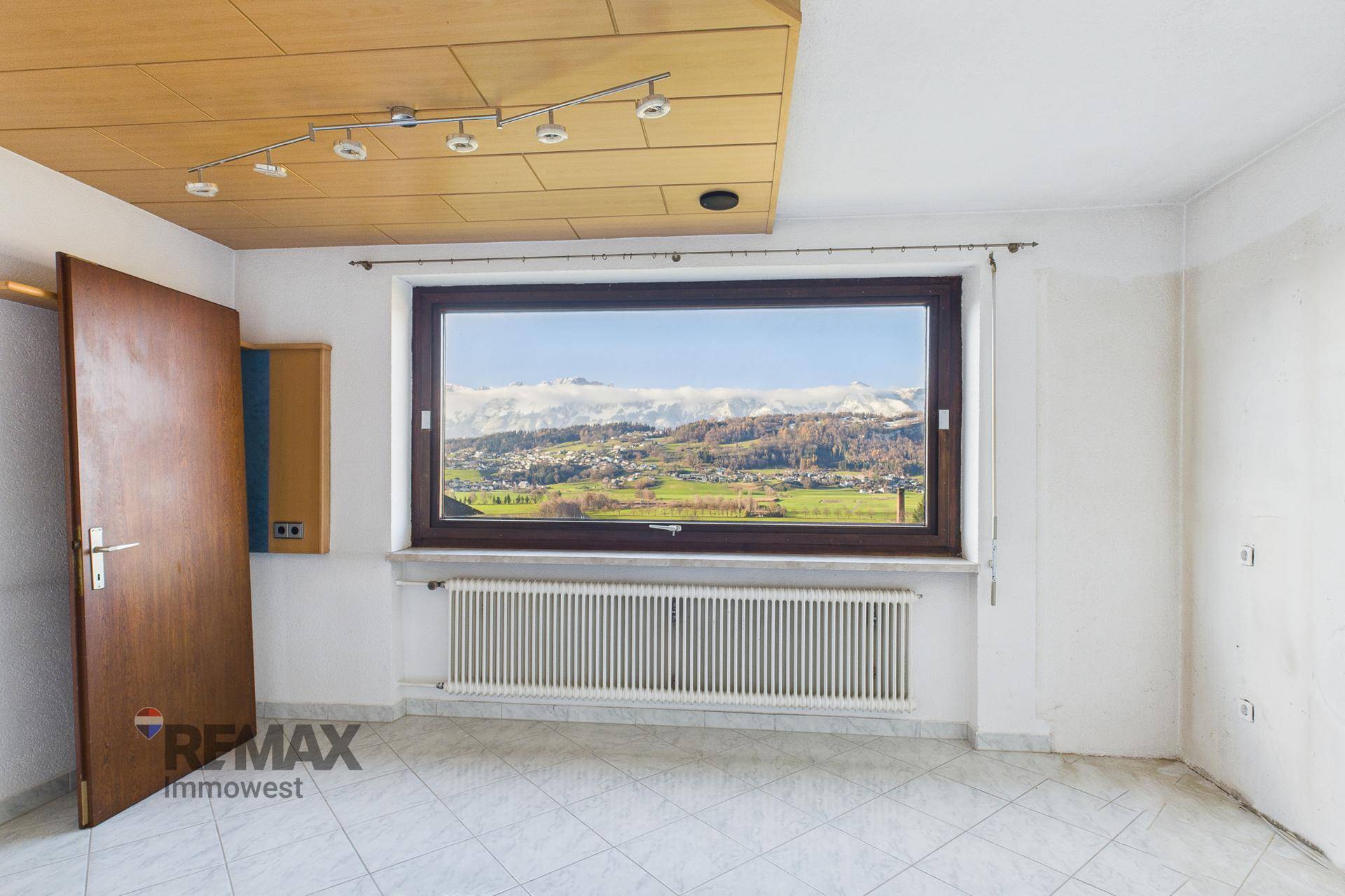 Heller Raum mit Fliesenboden und großem Fenster, das einen weiten Bergblick bietet.