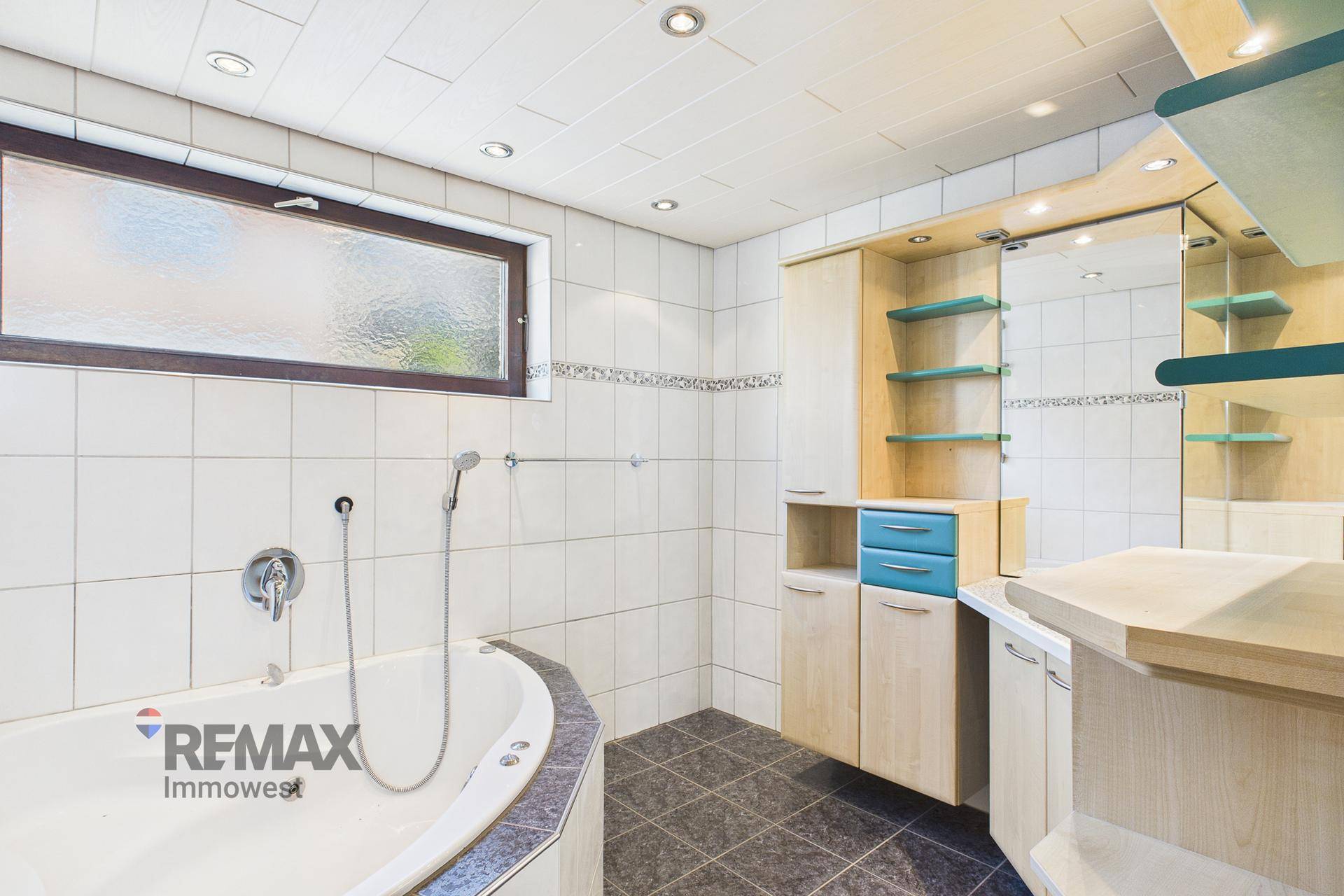 Badezimmer mit Eckbadewanne, Duschkopf und modernen Einbauschränken in hellen Farben.