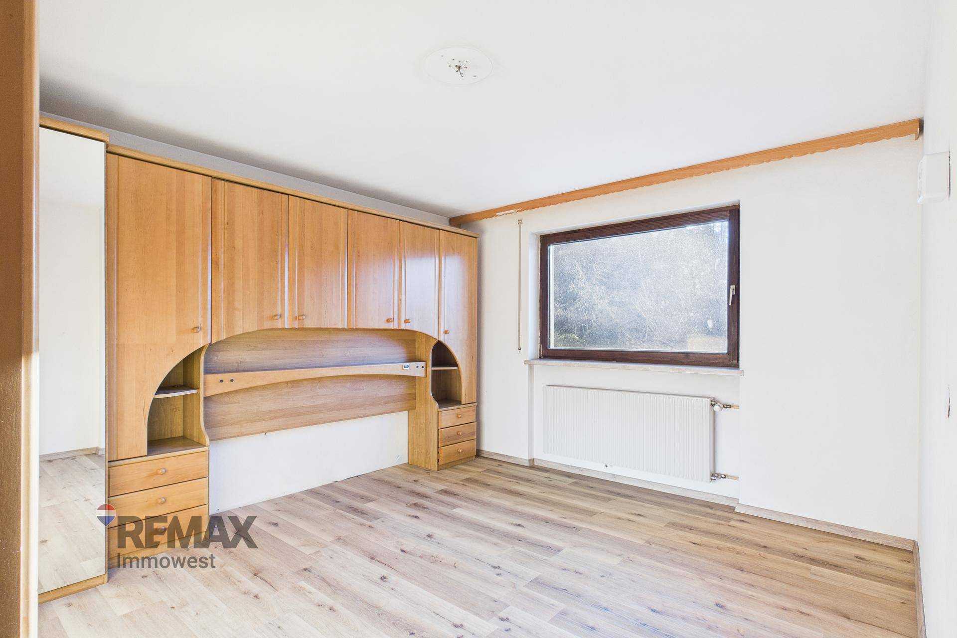 Schlafzimmer mit Einbauschränken aus Holz und Fenster, das eine gemütliche Atmosphäre schafft.