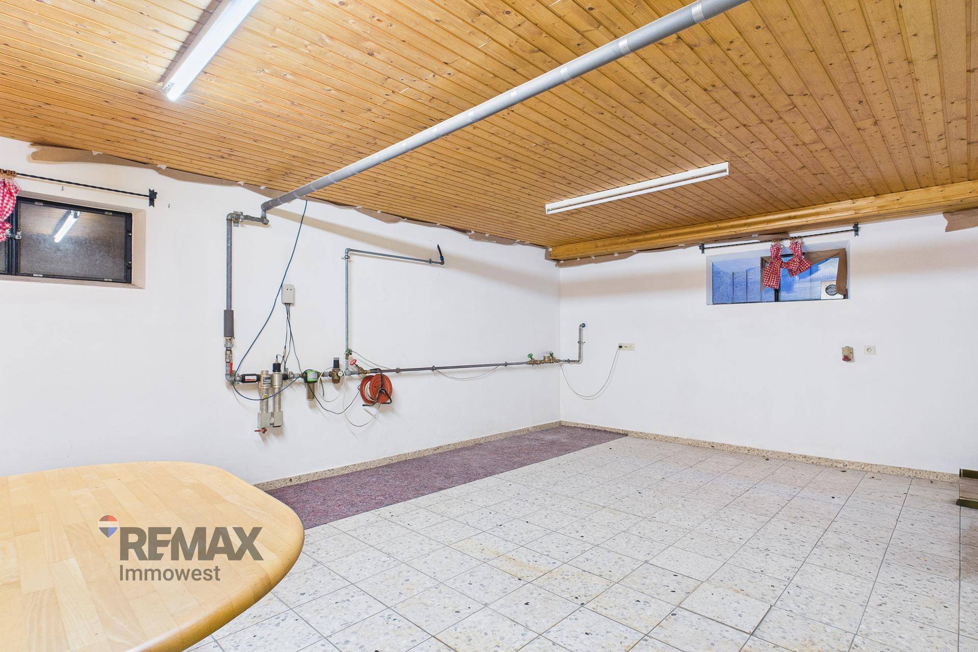Geräumiger Hauswirtschaftsraum mit Fliesenboden, Holzdecke und sichtbaren Installationen an der Wand.