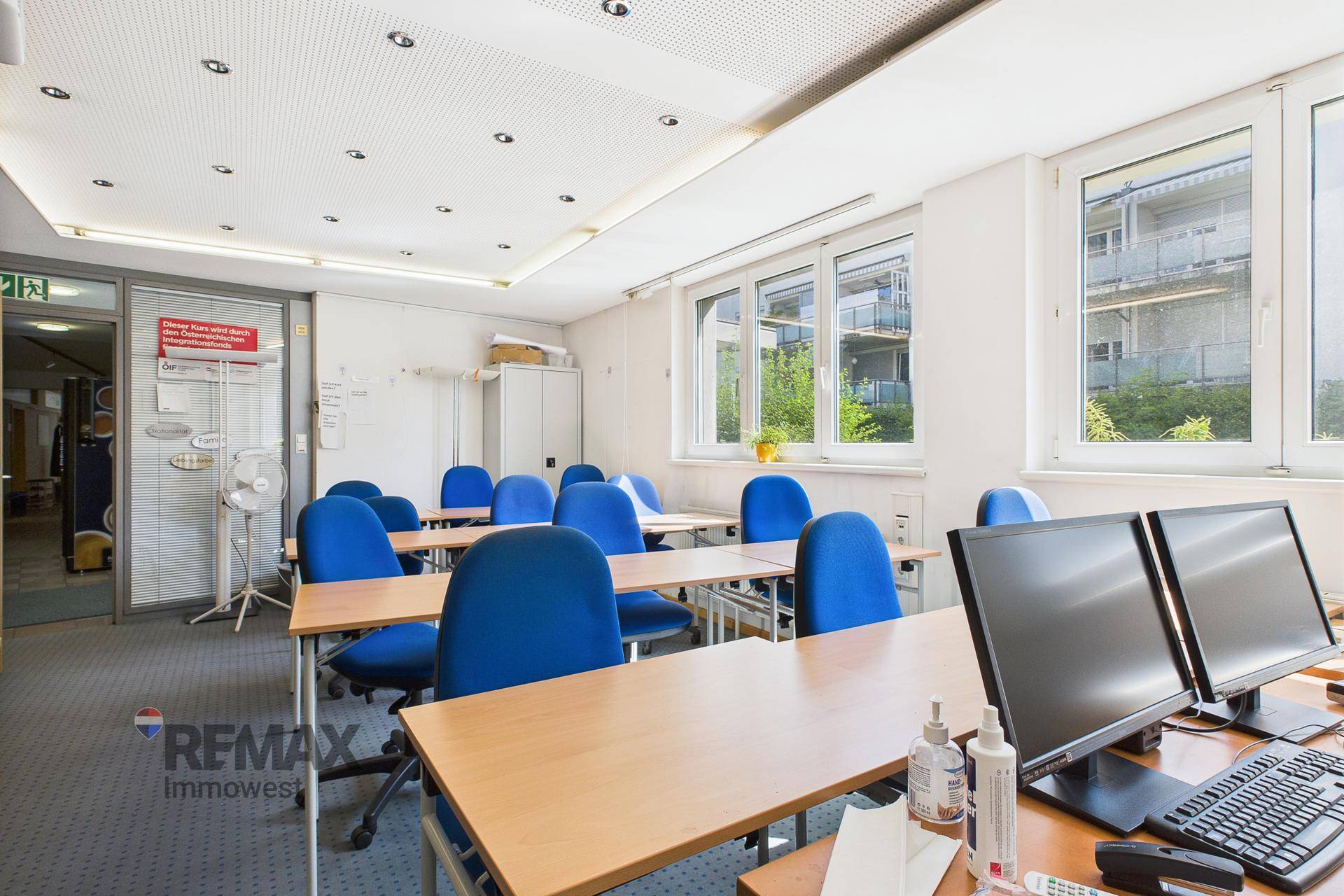 Schulungsraum mit Computern, blauen Stühlen und Holztischen, ausgestattet für Lernzwecke und Gruppenarbeiten.