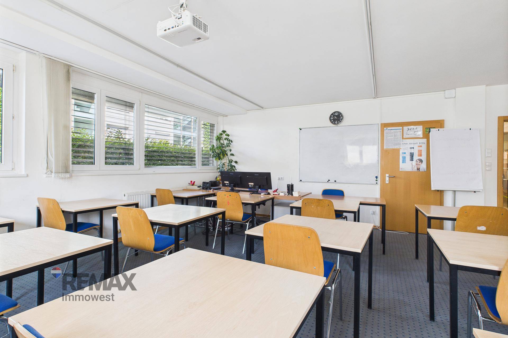 Schulungsraum mit Tischen, Stühlen, Whiteboard und Deckenprojektor, bereit für Präsentationen und Unterricht.