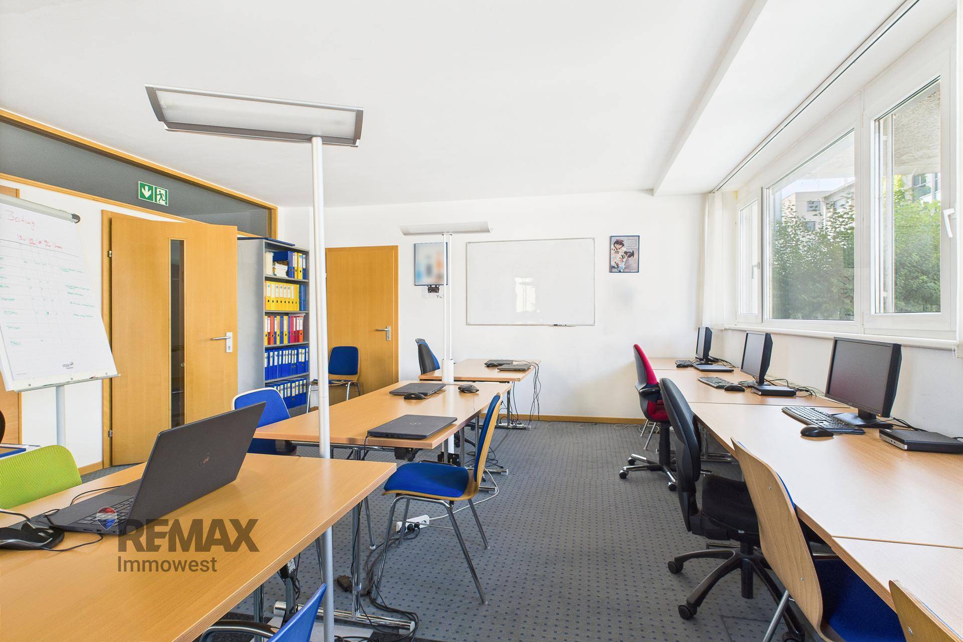 Computerraum mit mehreren Arbeitsplätzen, Whiteboards und Fenstern, gut beleuchtet und funktional eingerichtet.