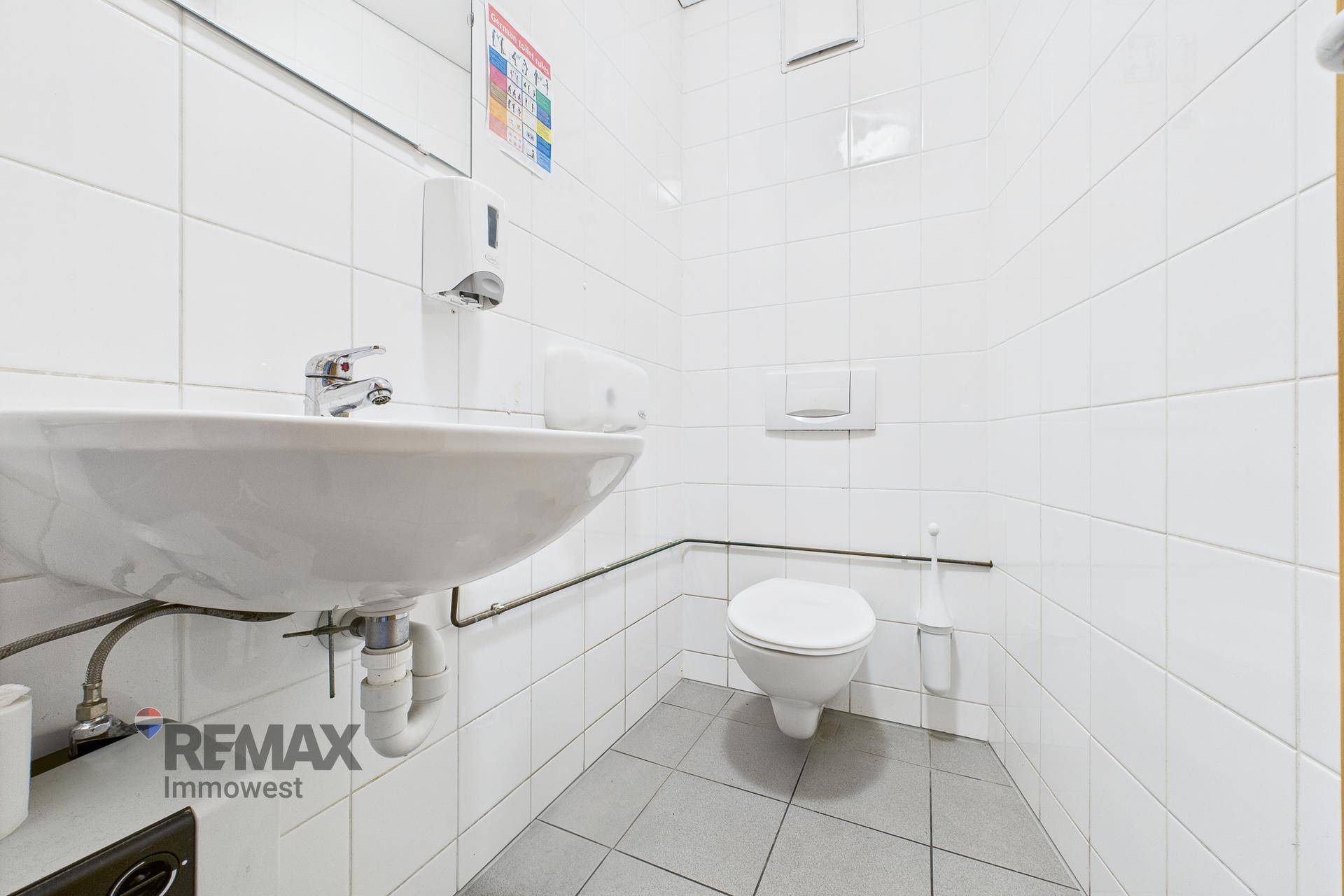 Saubere Toilette mit weißen Fliesen, Waschbecken und WC, funktional und hell eingerichtet.