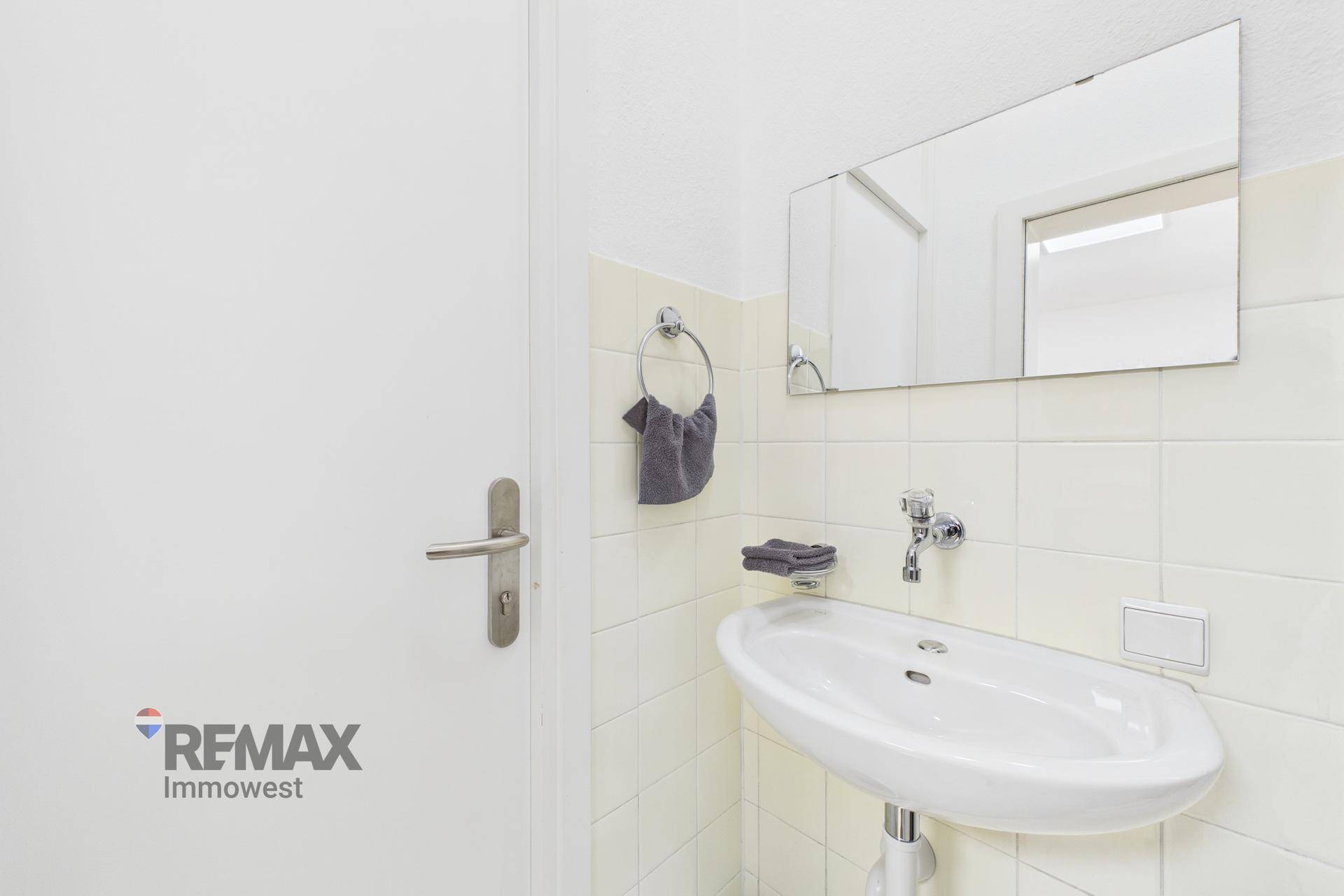 Helles Badezimmer mit Waschbecken, Spiegel und hell gefliesten Wänden.