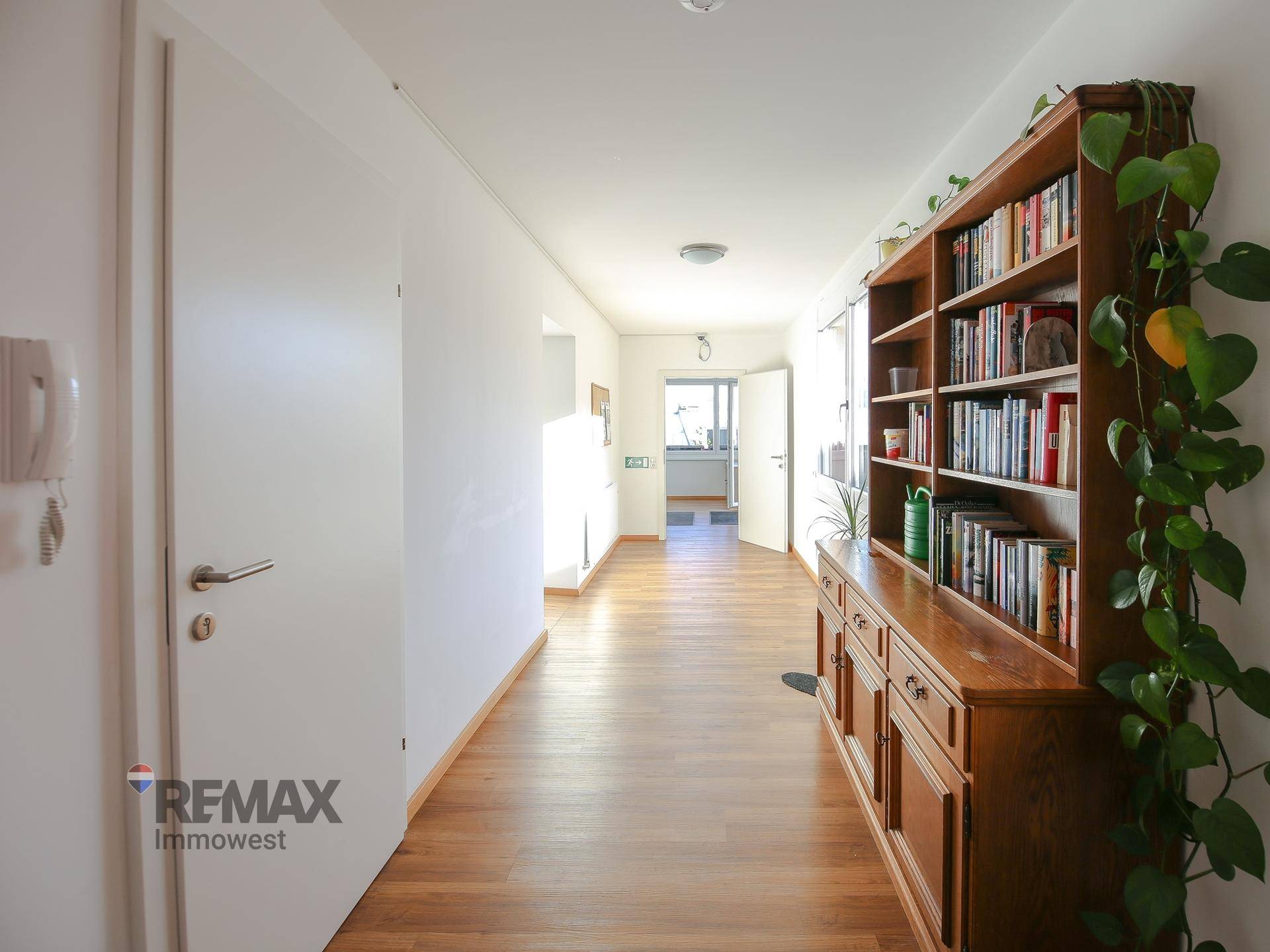 Langer Flur mit Holzboden, Bücherregal und viel natürlichem Licht.