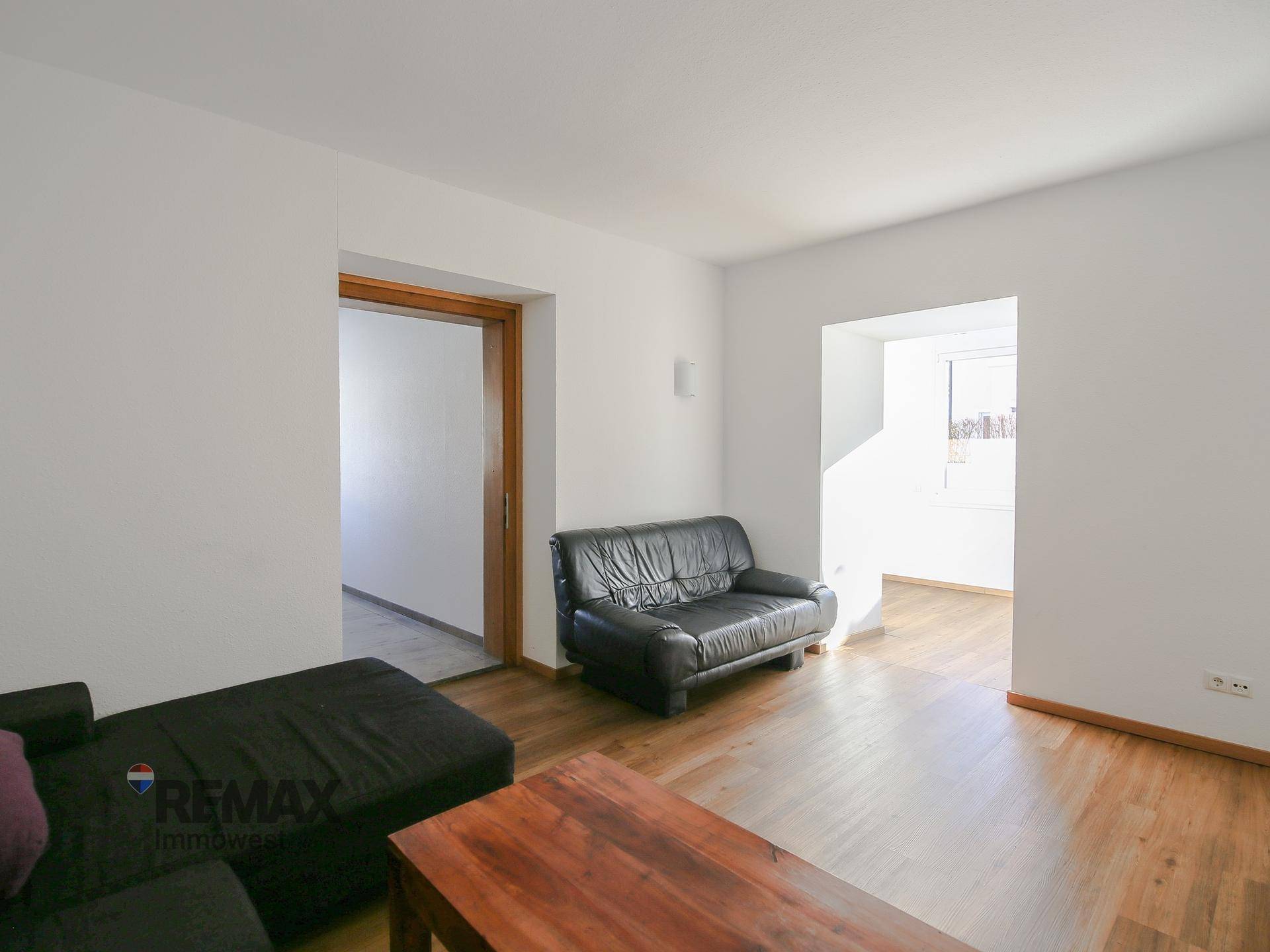 Helles Wohnzimmer mit Holzboden und Zugang zu weiteren Räumen.