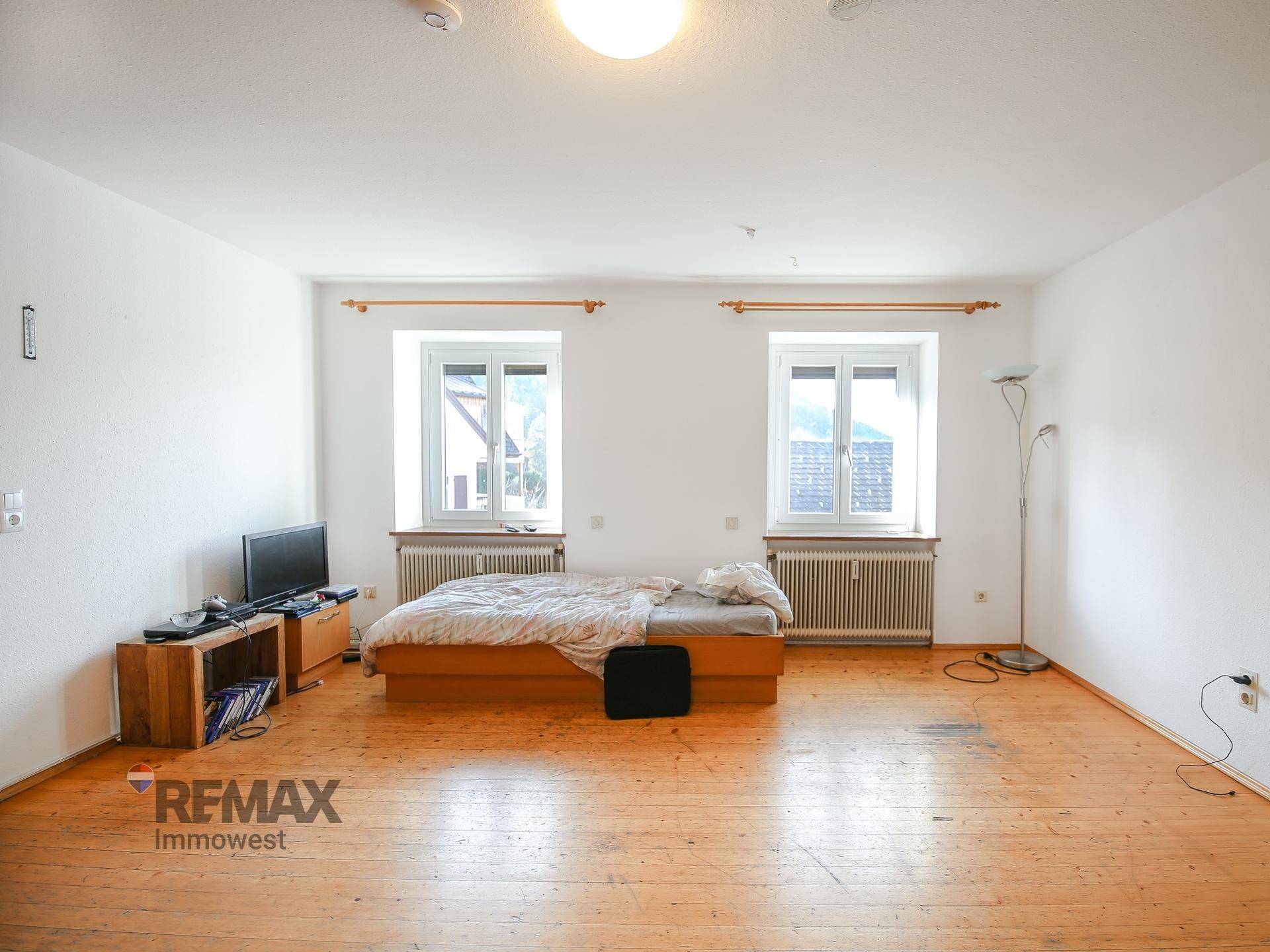Helles Schlafzimmer mit Holzboden, zwei Fenstern und Heizkörpern.