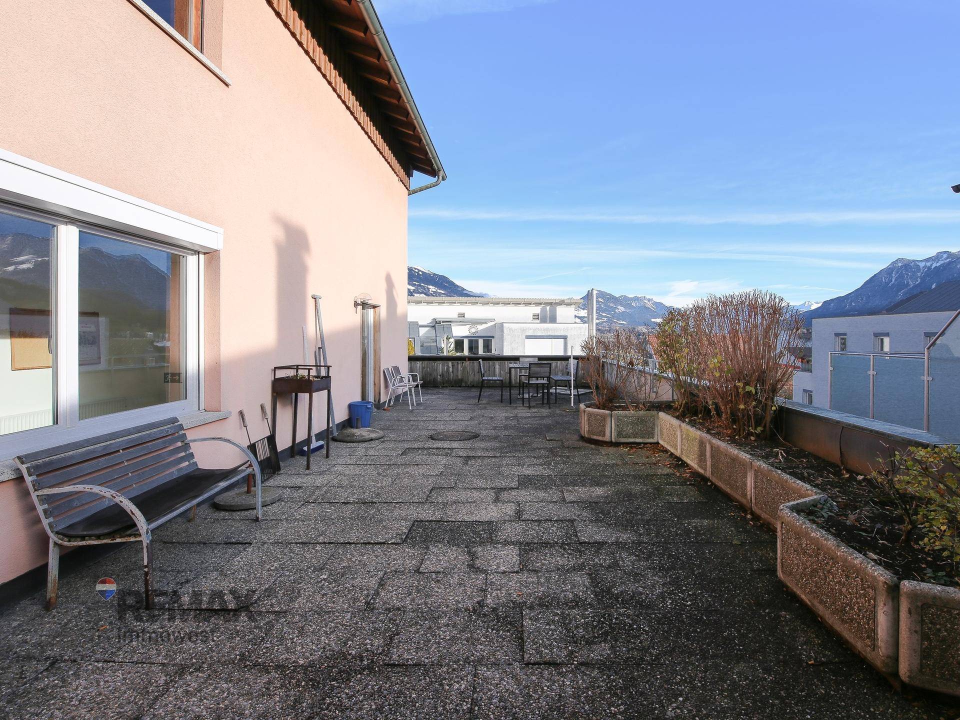 Weitläufige Terrasse mit Bergblick, Sitzbank und Pflanzkübeln.