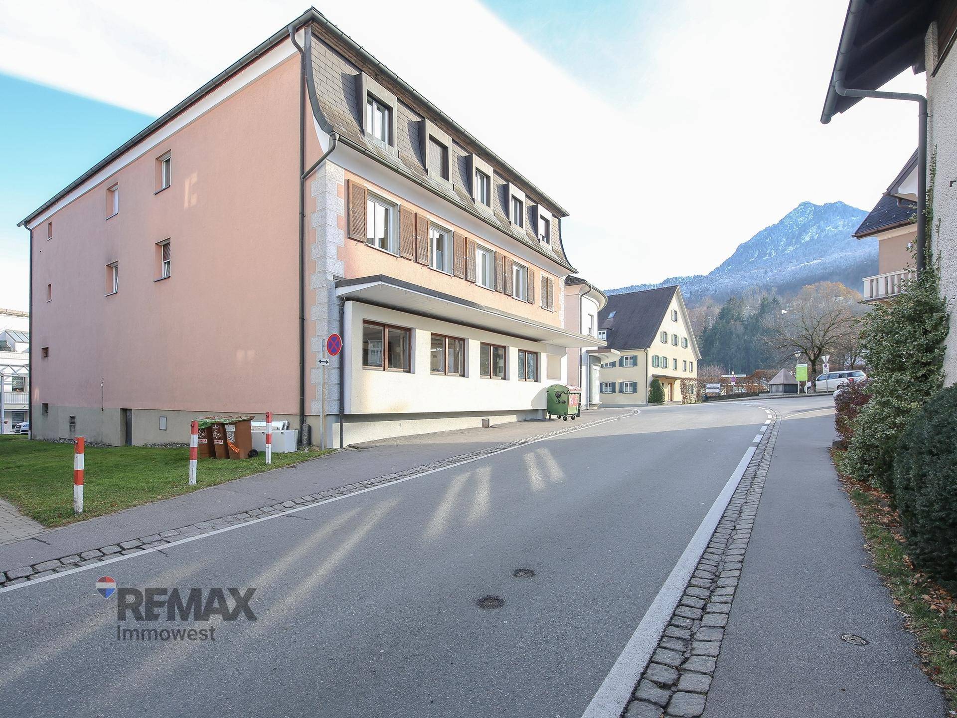 Gebäudeansicht von der Straße mit Mansarddach und umliegender Berglandschaft.