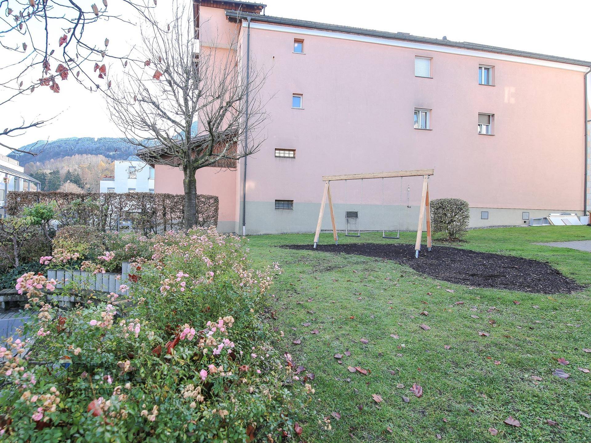 Grüner Gartenbereich mit Schaukel, Rosenbeeten und Hecke.