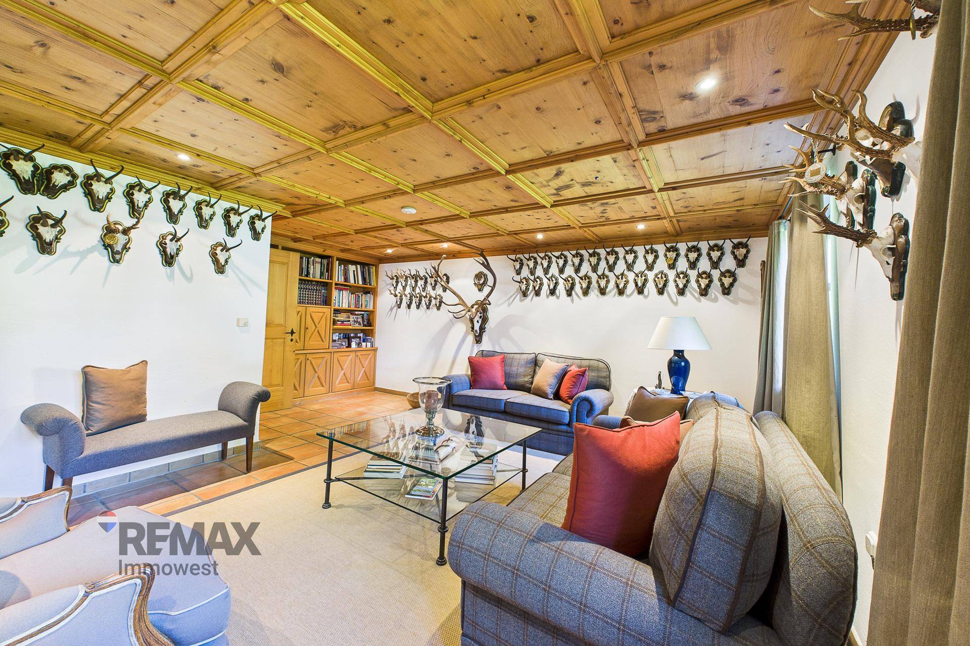 Geräumiges Wohnzimmer im alpinen Stil mit Holzkassettendecke, bequemen Sofas und Jagdtrophäen.