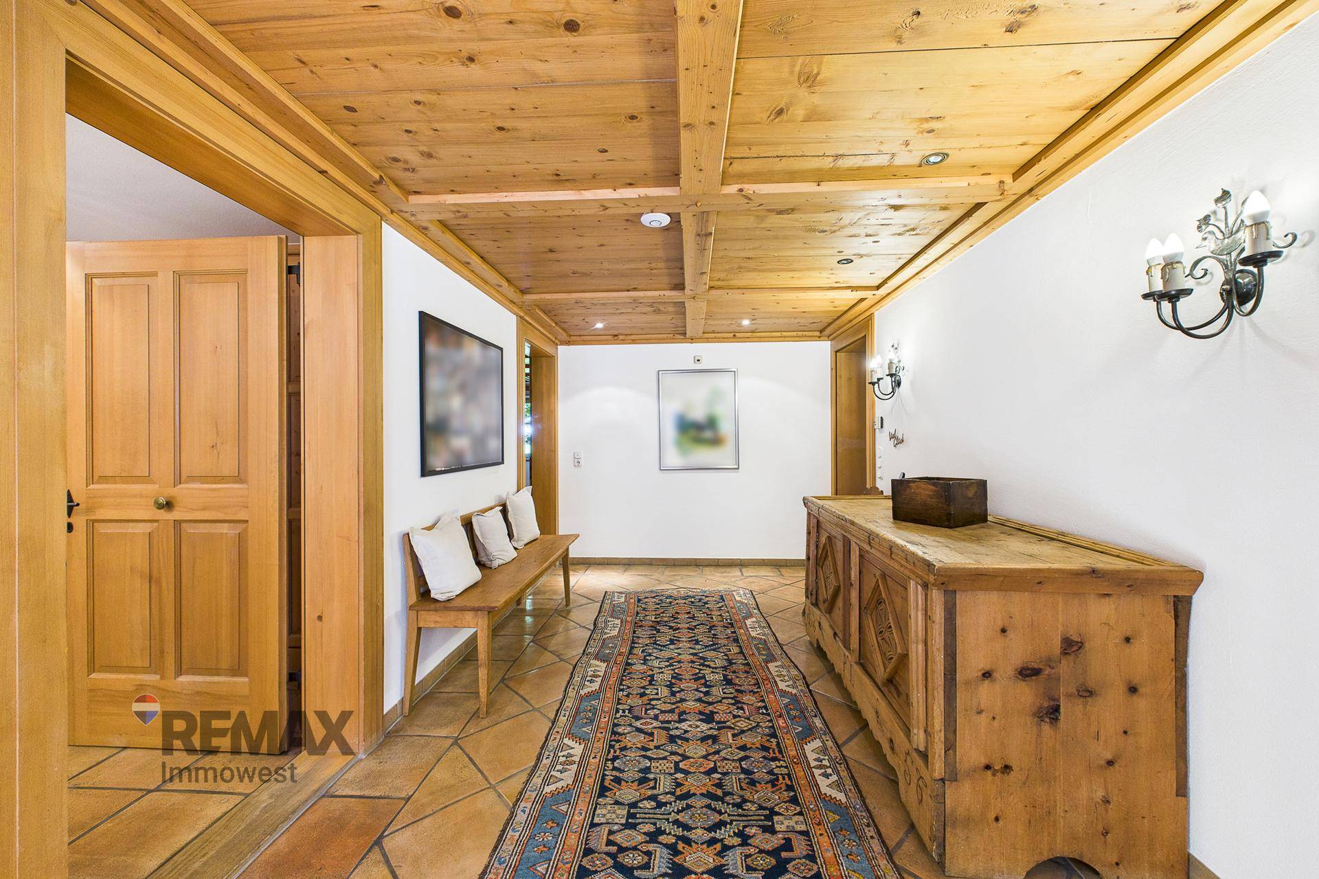 Langer Flur mit Holzbalkendecke, rustikalen Holzmöbeln und traditionellem Teppichläufer.