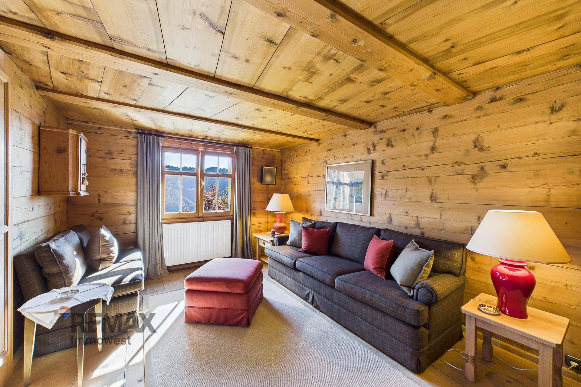 Gemütliches Wohnzimmer mit Holzwänden und -decke, bequemen Sofas und Blick ins Grüne.