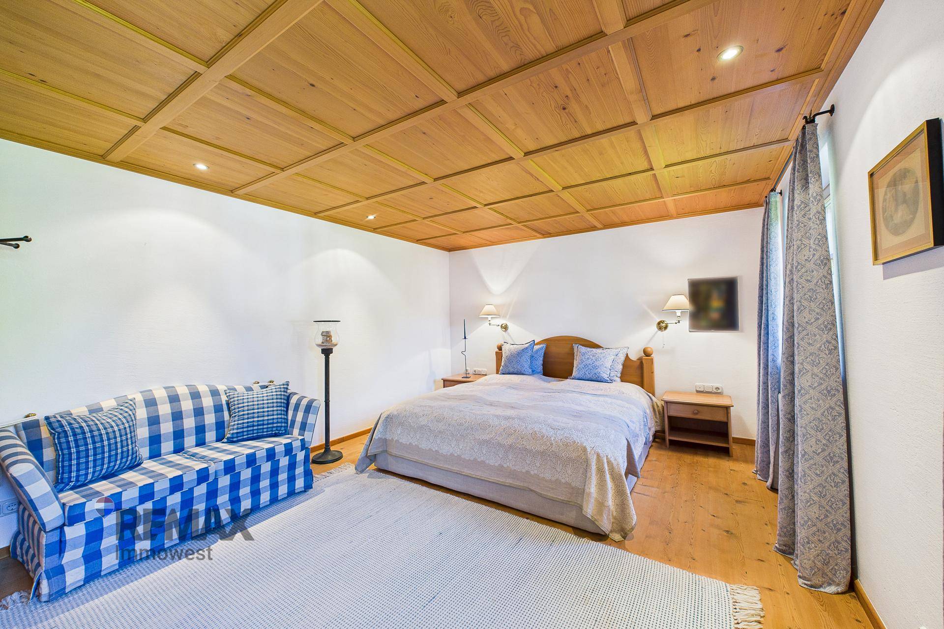 Helles Schlafzimmer mit Holzkassettendecke, Doppelbett und kariertem Sofa in Blau und Weiß.