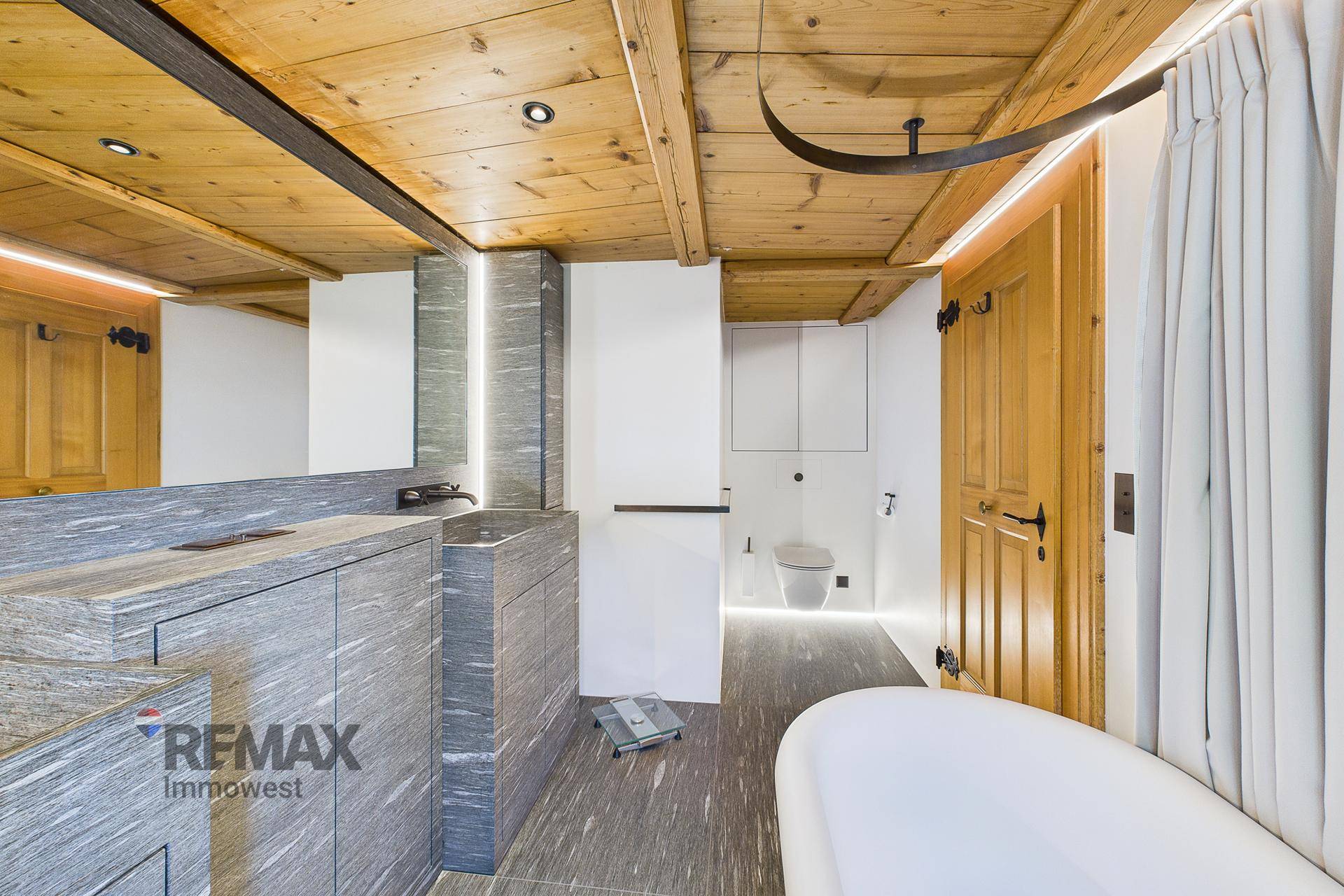 Modernisiertes Badezimmer mit Holzbalkendecke, Steinfliesen und freistehender Badewanne.