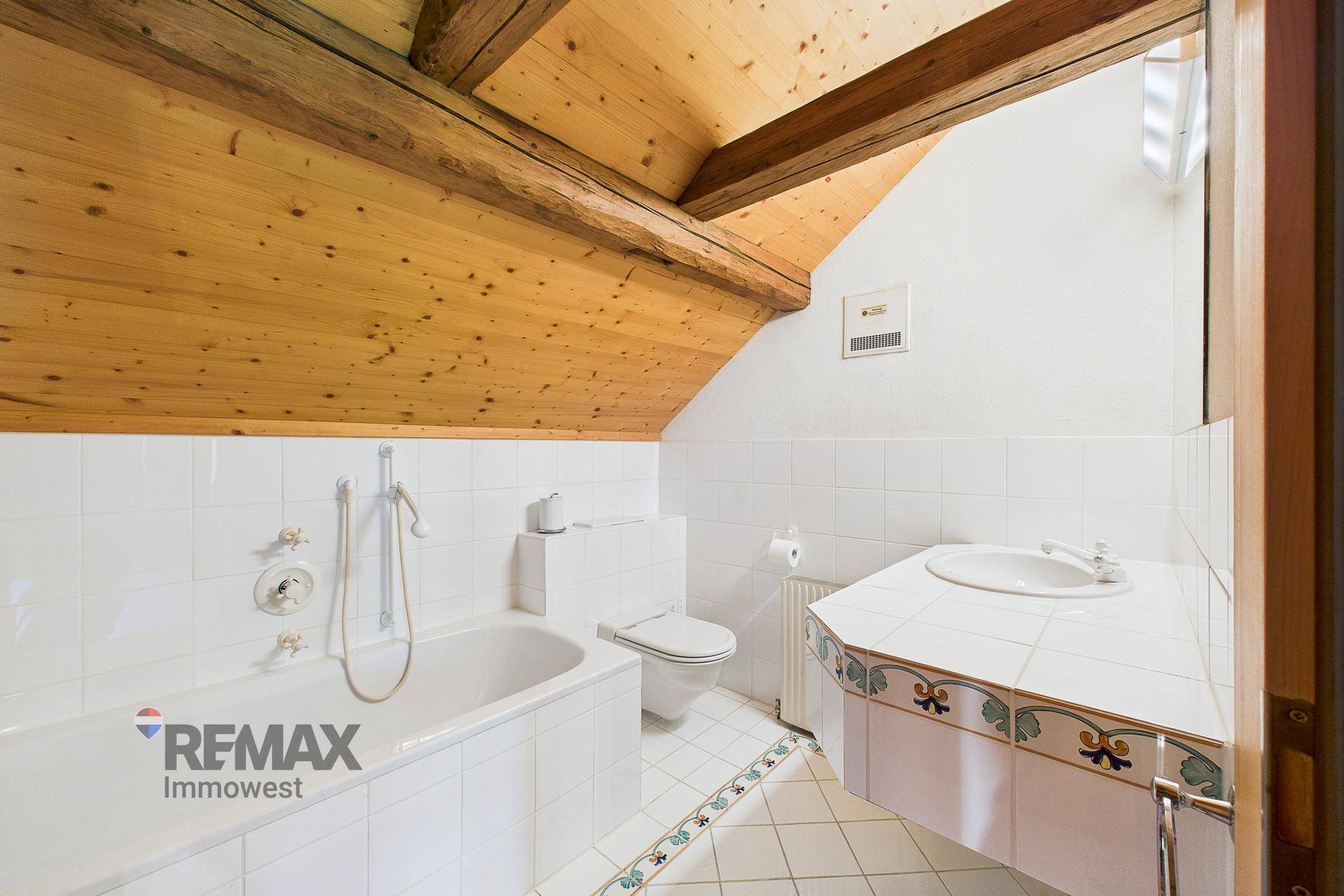 Badezimmer im Dachgeschoss mit Badewanne, WC und Waschtisch unter der schrägen Holzdecke.