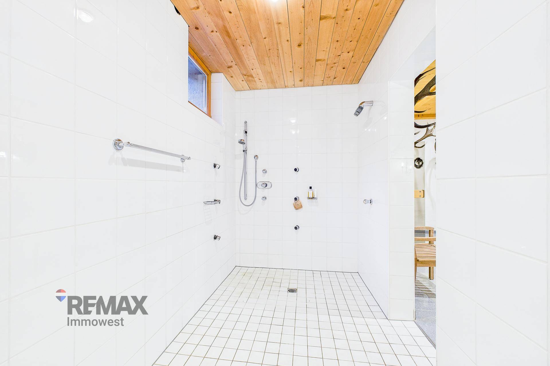 Geräumige Dusche mit weißen Fliesen, zwei Duschköpfen und einer Holzdecke für ein natürliches Ambiente.