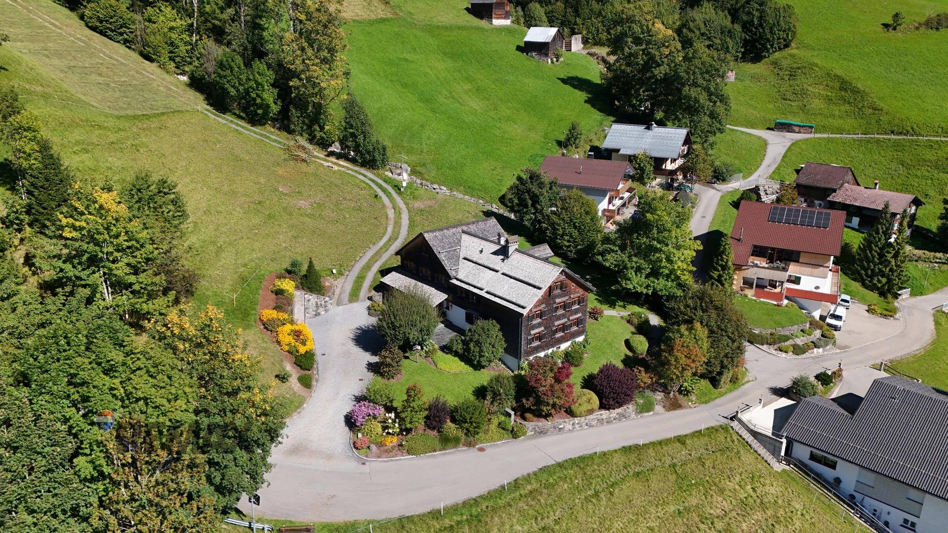 Luftaufnahme des Anwesens mit umliegenden Häusern und üppiger grüner Landschaft in den Bergen.