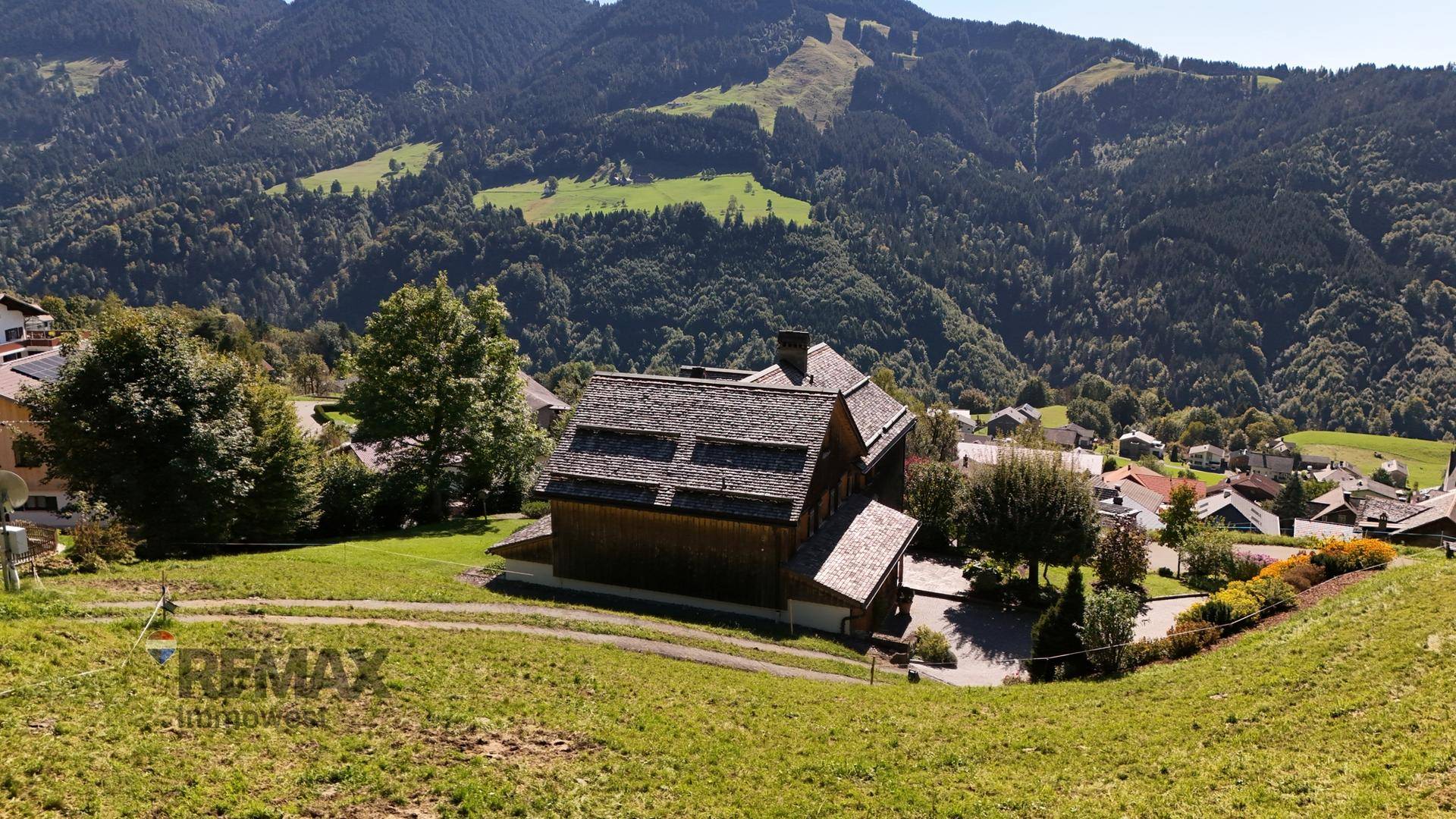 Traditionelles Holzhaus in alpiner Hanglage mit weitem Blick auf die umliegende Berglandschaft.