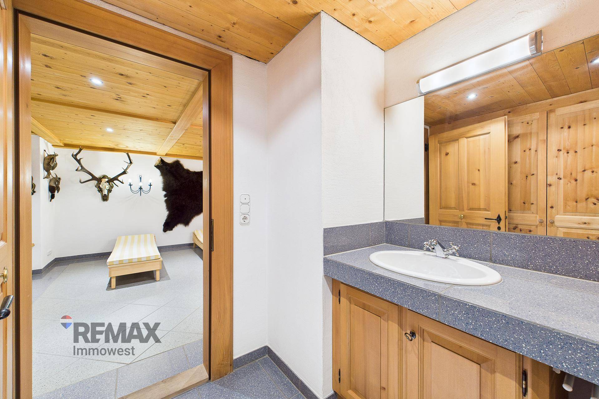 Badezimmer mit Einzelwaschbecken, Holzunterschrank und Blick in den angrenzenden Entspannungsbereich.