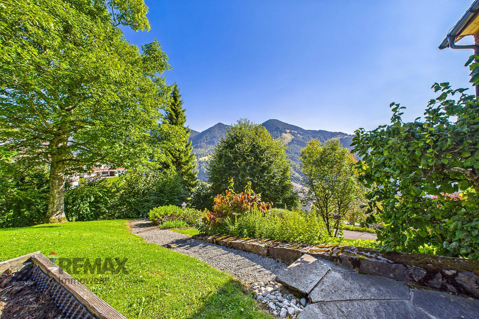 Gepflegter Gartenweg mit Steinstufen und einem weiten, sonnigen Blick auf die umliegenden Berge.