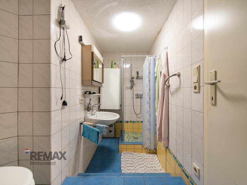 Helles Badezimmer mit blauen und gelben Fliesen, Dusche und Einzelwaschbecken.