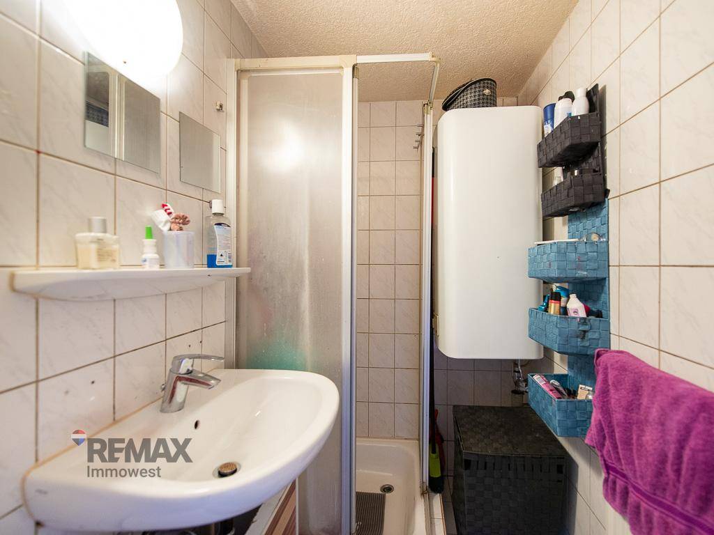 Kleines Badezimmer mit Dusche, Waschbecken und weiß gefliesten Wänden.