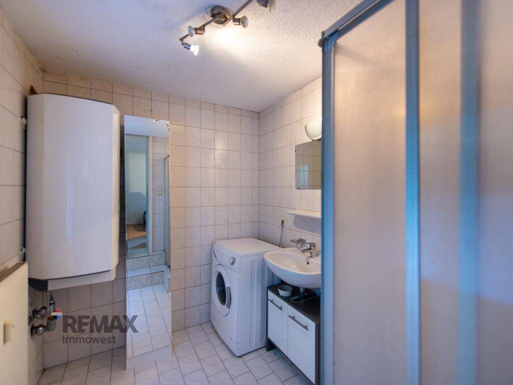 Badezimmer mit Waschmaschine, Dusche und weiß gefliesten Wänden.