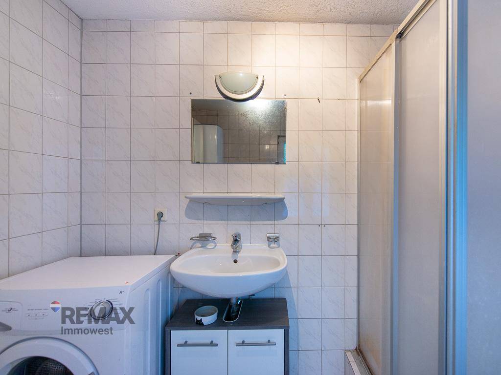Funktionales Badezimmer mit Waschbecken, Spiegel und weiß gefliesten Wänden.