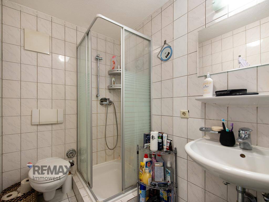 Helles Badezimmer mit Duschkabine, WC und Waschbecken, komplett gefliest in neutralen Farben.