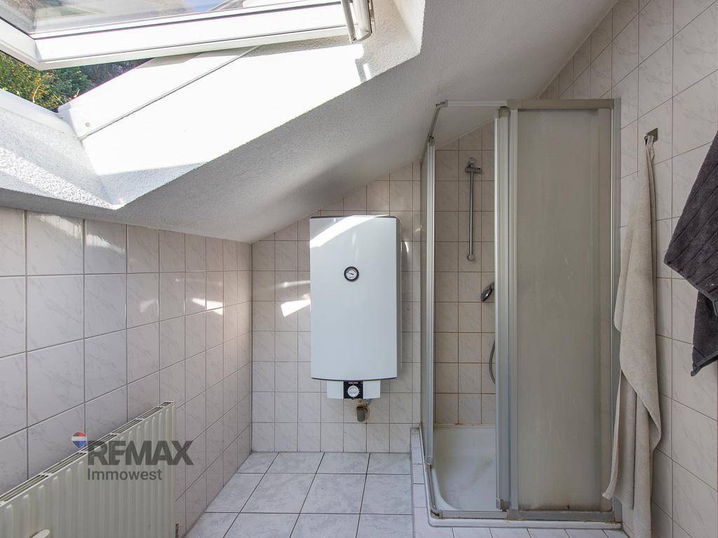 Dachgeschoss-Badezimmer mit Duschkabine, Dachfenster und Warmwasserbereiter, vollständig gefliest.