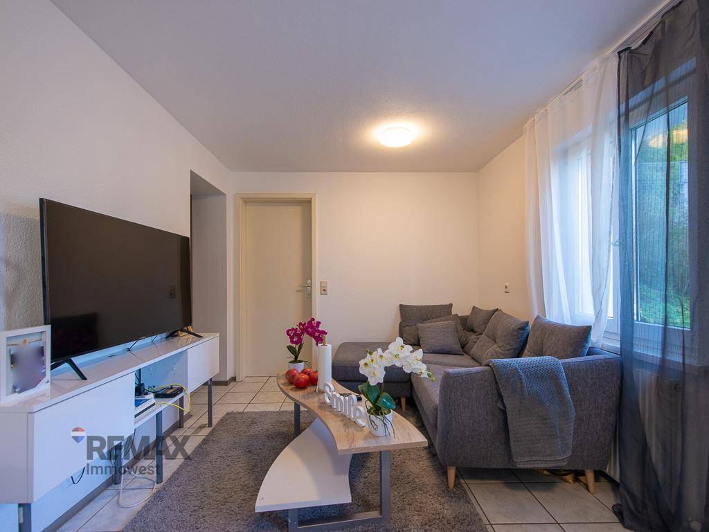 Gemütlicher Wohnbereich mit grauem Ecksofa, Couchtisch und Fernseher, ausgestattet mit Fliesenboden.