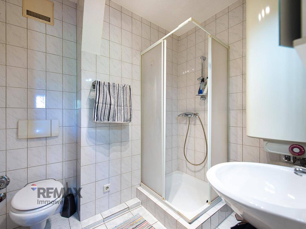 Gefliestes Badezimmer mit Duschkabine, WC und Waschbecken, praktisch und pflegeleicht gestaltet.