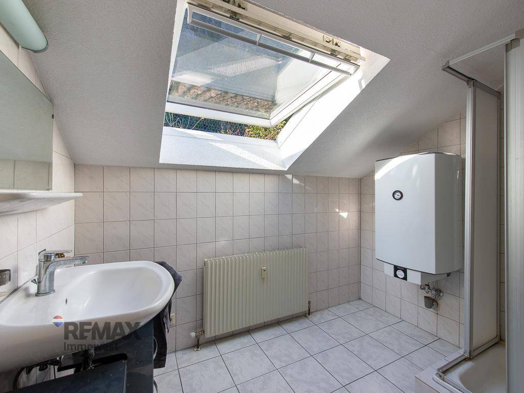 Helles Badezimmer im Dachgeschoss mit Dachfenster, Waschbecken und Heizkörper, komplett gefliest.