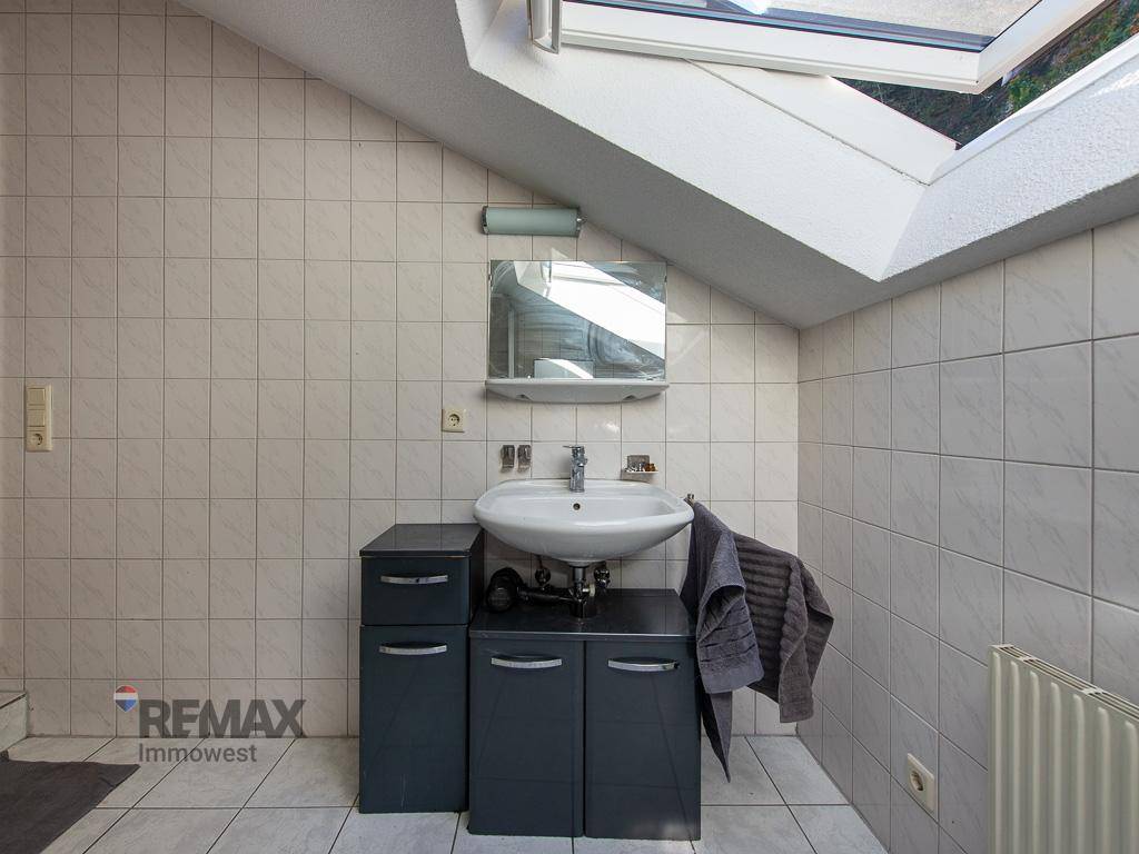 Badezimmer im Dachgeschoss mit Dachfenster, Waschbecken und Unterschrank, gefliest in hellen Tönen.
